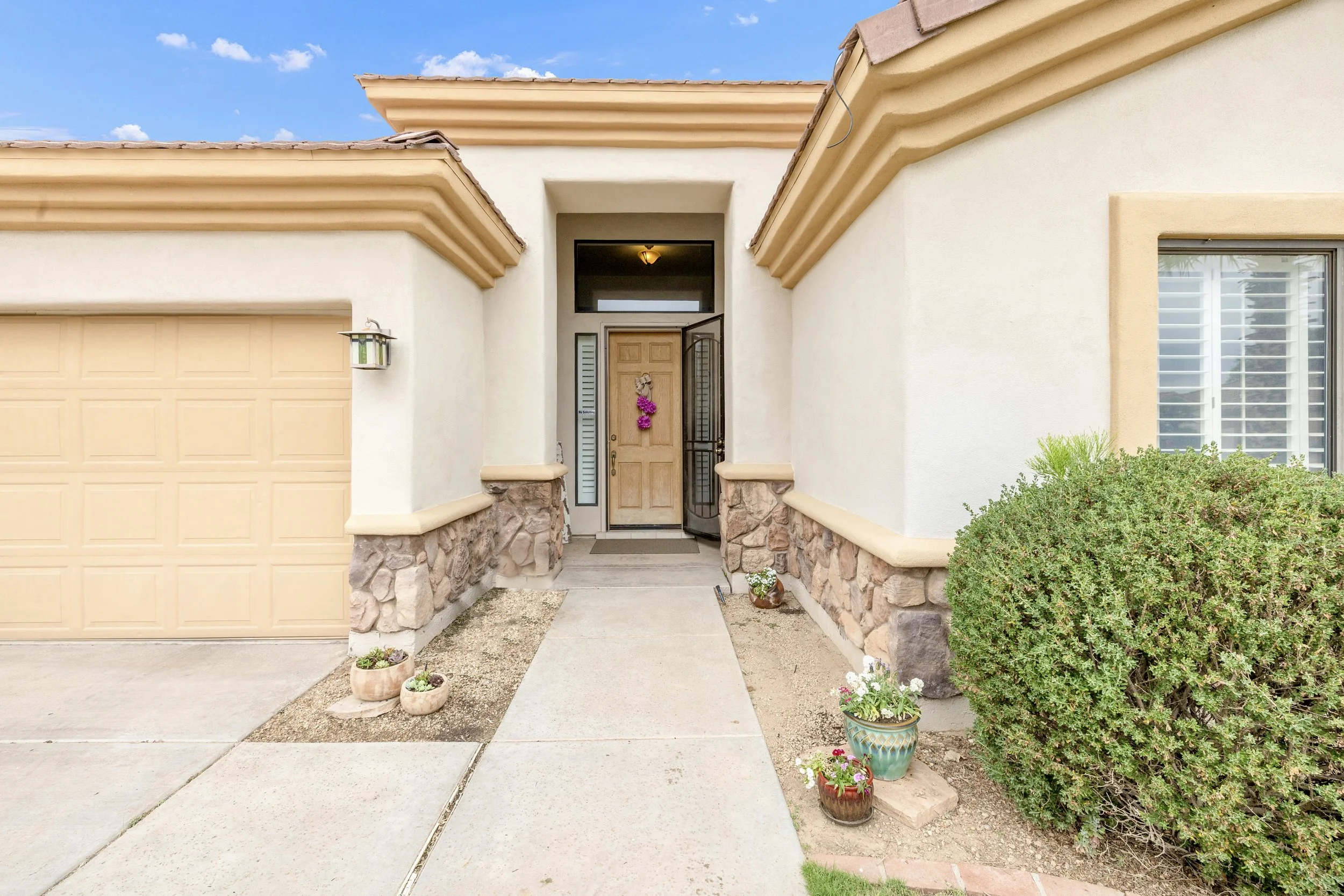 This front entry exterior in Goodyear, AZ showcases inviting design with stone accents and a bright wooden door, perfect for real estate photography highlighting curb appeal.