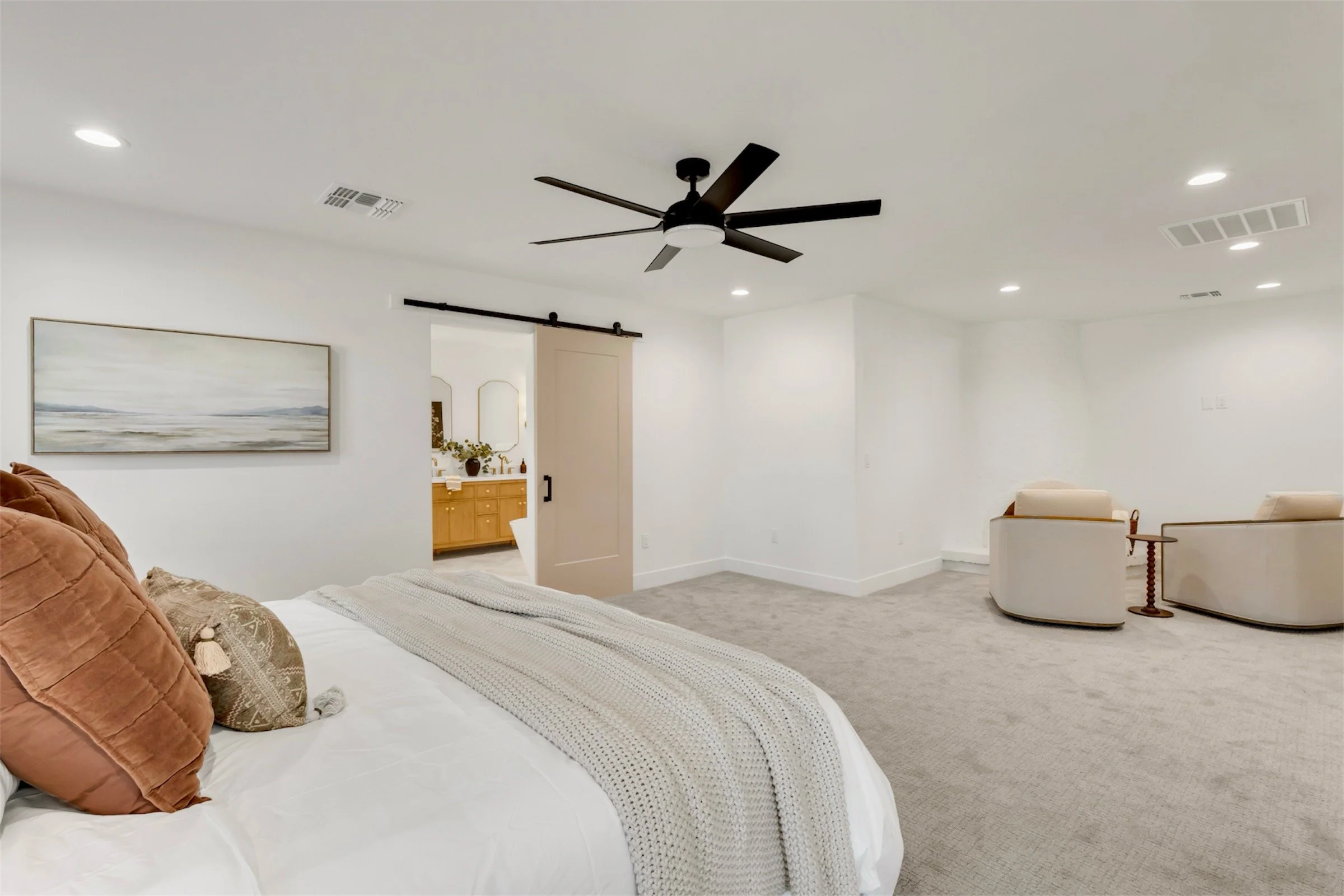 Spacious primary bedroom in Phoenix, AZ featuring a seating area, neutral tones, and a sliding barn door to the ensuite bathroom.