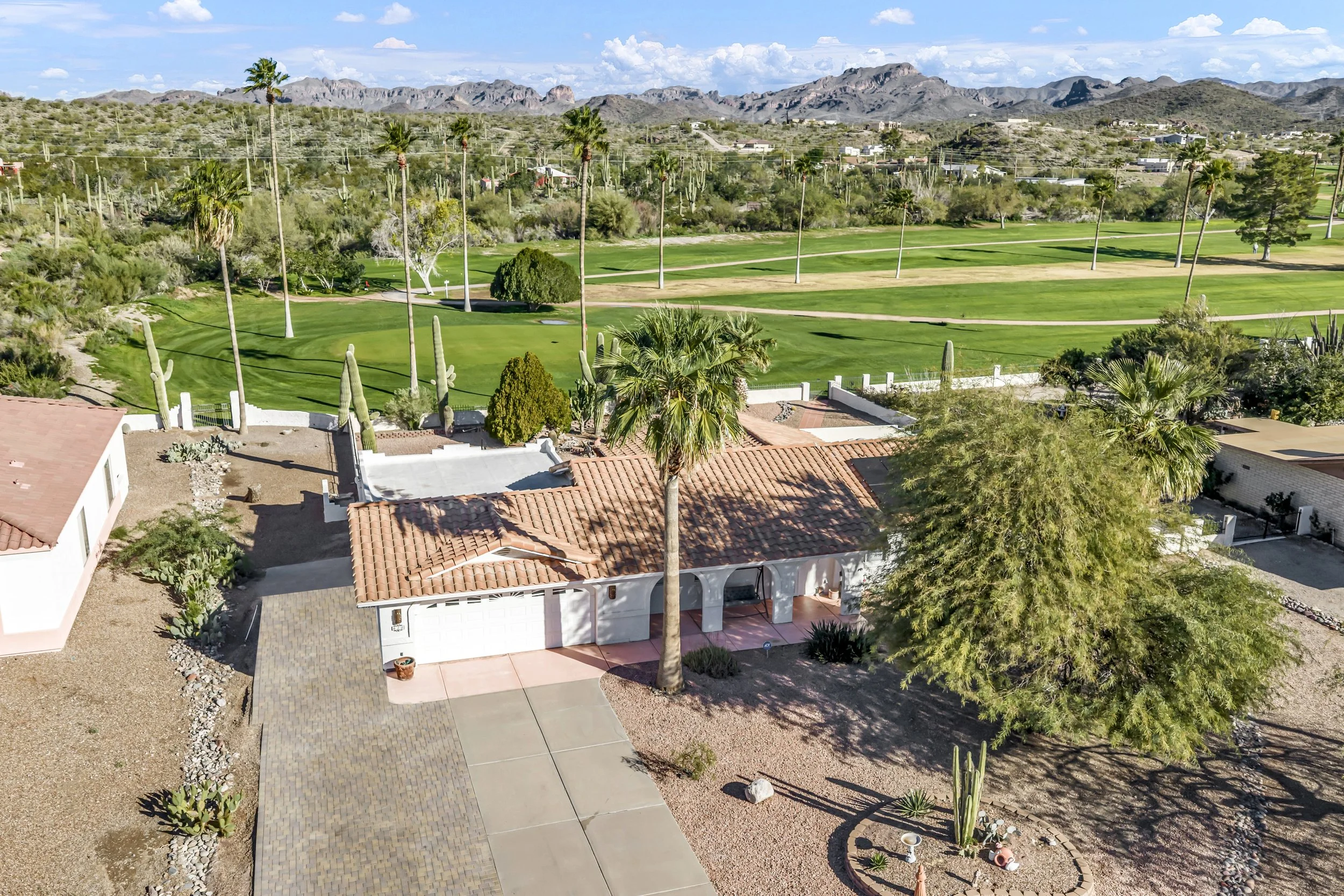 Drone aerial view of an Arizona golf course community with green fairways, palm trees, desert landscaping, and nearby homes.