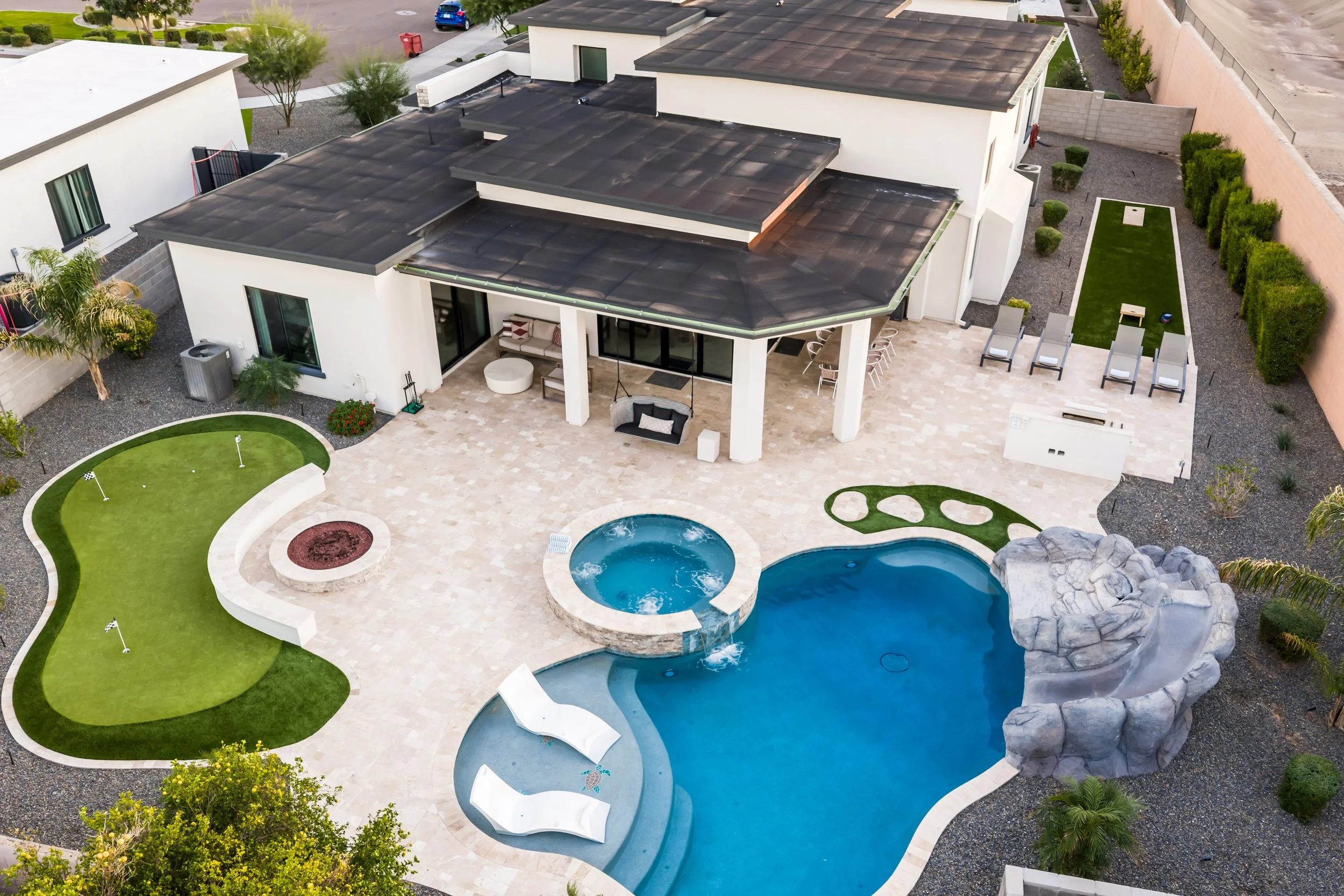 Aerial drone view of a luxury Arizona backyard featuring a swimming pool, raised spa, artificial putting green, and covered patio.