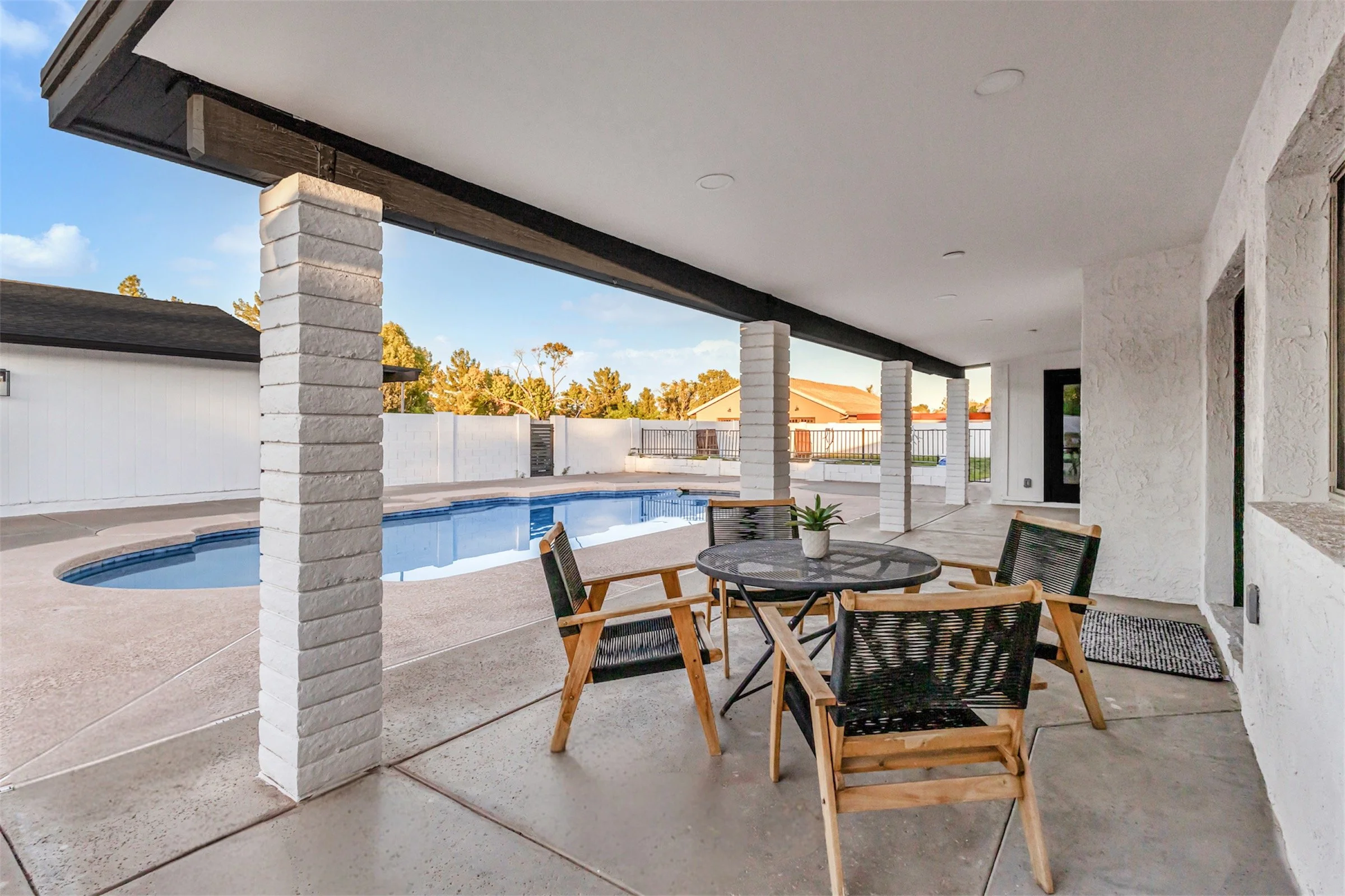 Outdoor covered patio with table and chairs overlooking pool in a stylish Phoenix, AZ backyard.