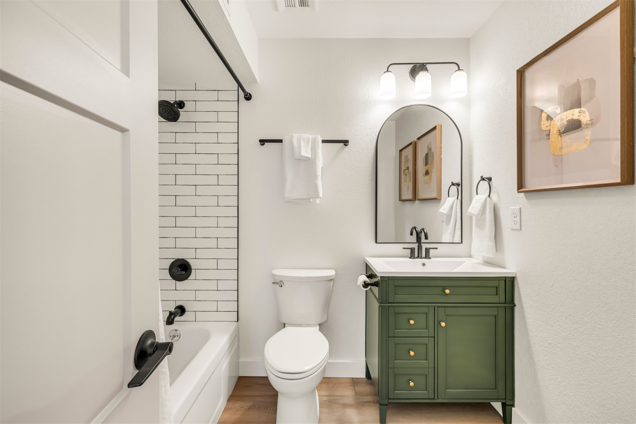 This modern bathroom in Mesa, AZ features a green vanity, white tub with black fixtures, and stylish decor, captured with expert real estate photography.