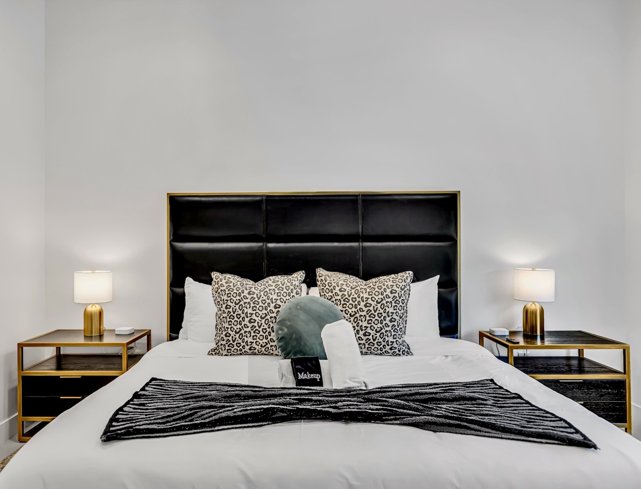 Bedroom with a black upholstered headboard, leopard accent pillows, and modern gold bedside lamps in Scottsdale, Arizona.