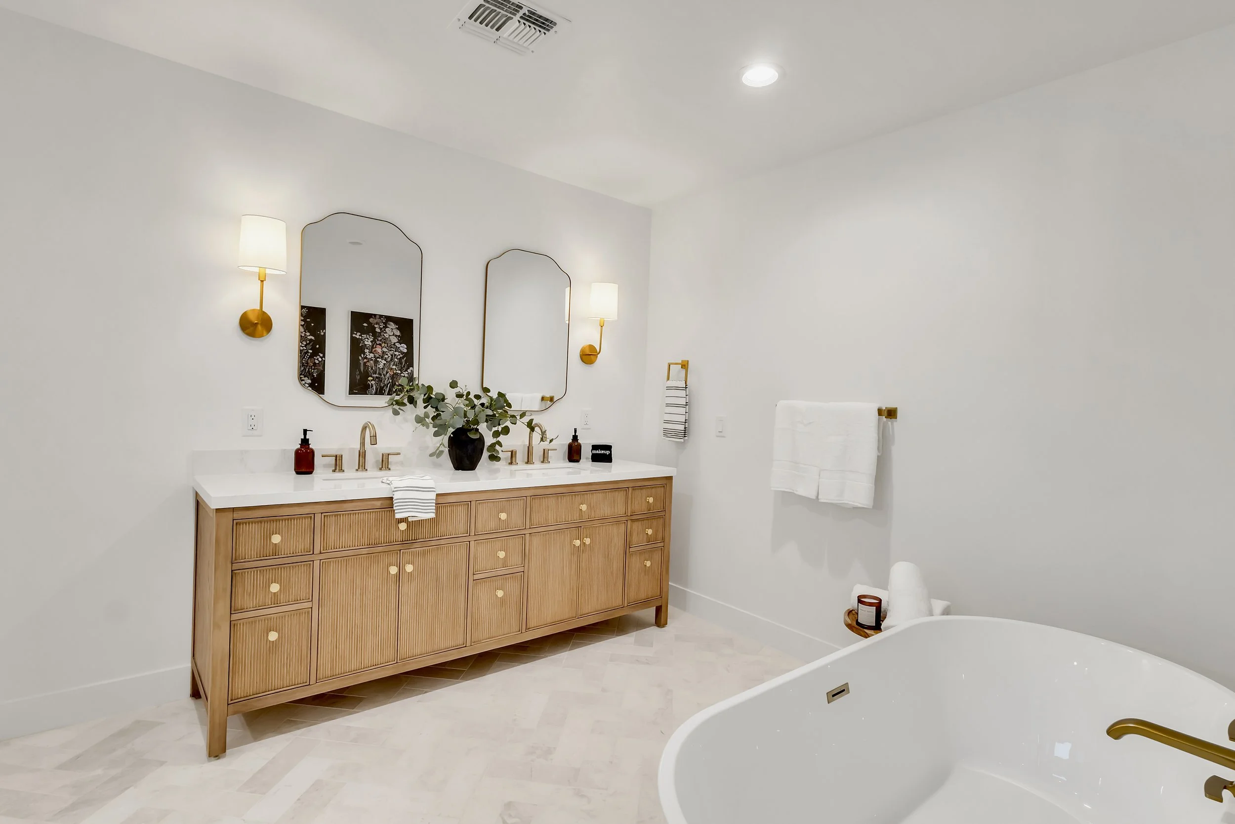 Bright bathroom in Phoenix, AZ featuring a freestanding tub, double vanity, and gold lighting fixtures with a spa-like atmosphere.
