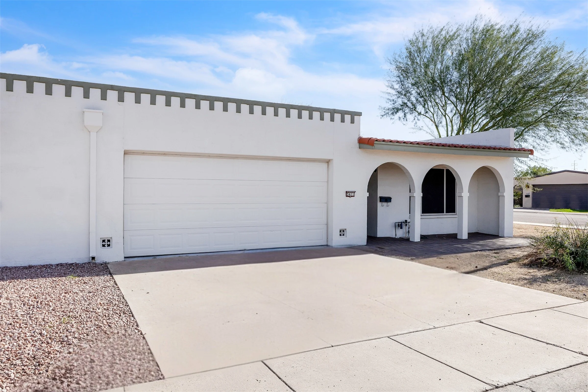 This real estate photography features a suburban home with a two-car garage and an arched porch in Tempe, AZ, showcasing its clean exterior and desert landscaping.