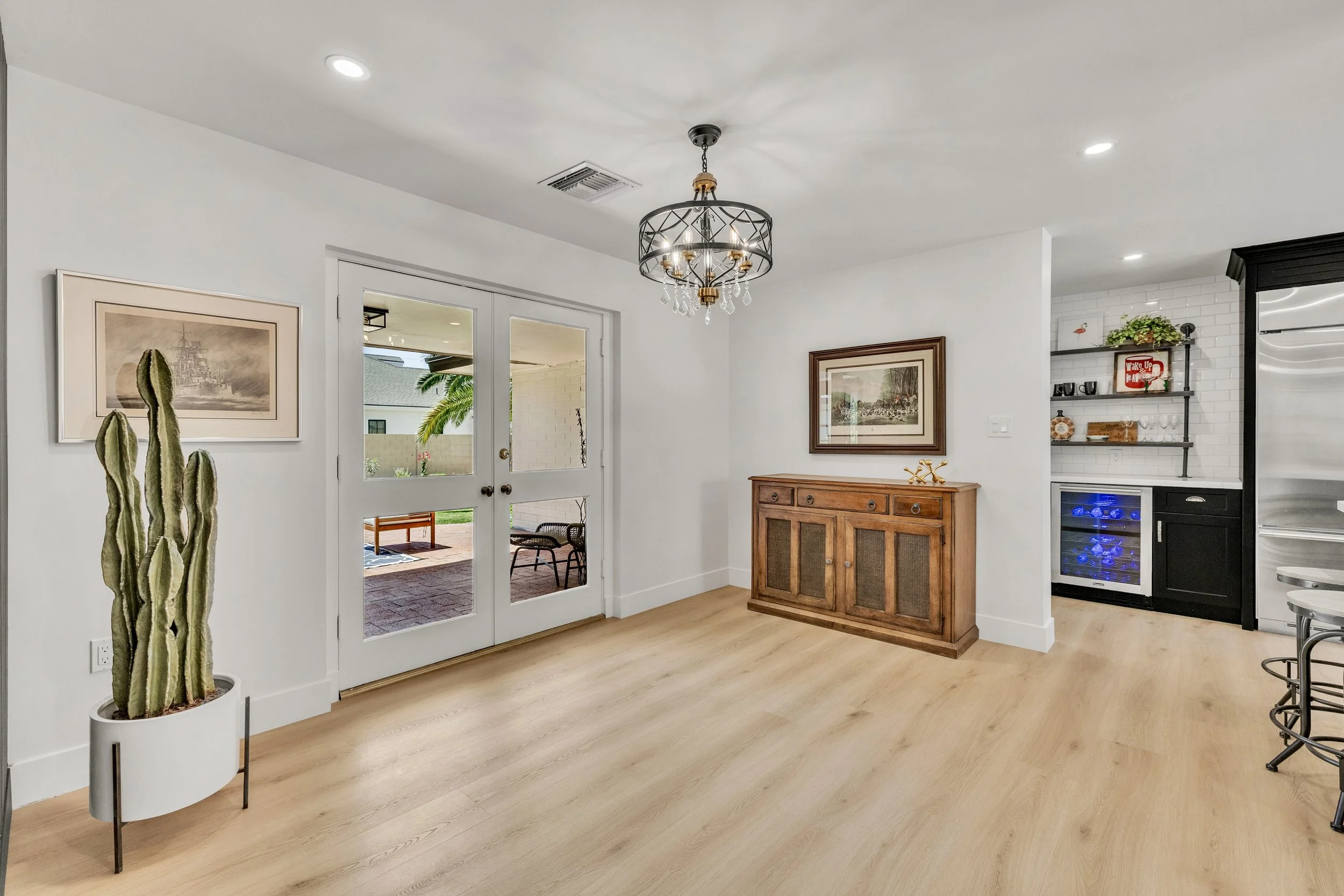 This interior dining area in Phoenix, AZ features light wood flooring, a decorative chandelier, and access to an outdoor patio, showcasing exceptional real estate photography.