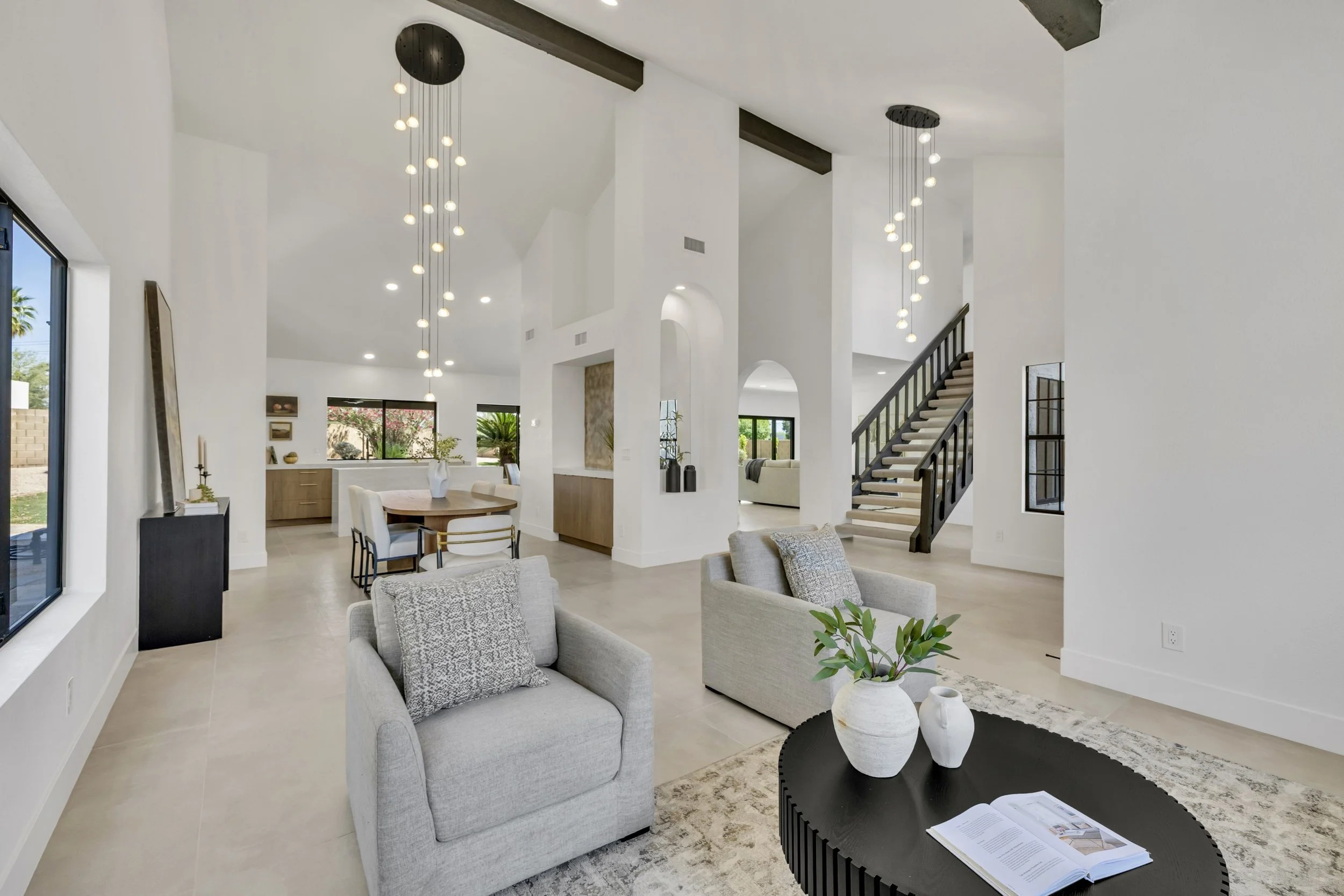 Spacious modern living room and dining area with staircase in a Scottsdale, AZ home, captured with professional real estate photography highlighting bright interiors and contemporary design.