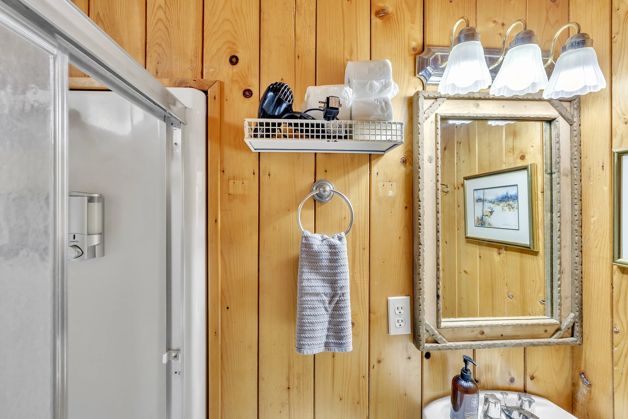 This Greer, AZ bathroom features rustic wood paneling, a mirror, mounted lights, and a towel ring, captured with professional real estate photography for a cozy cabin feel.