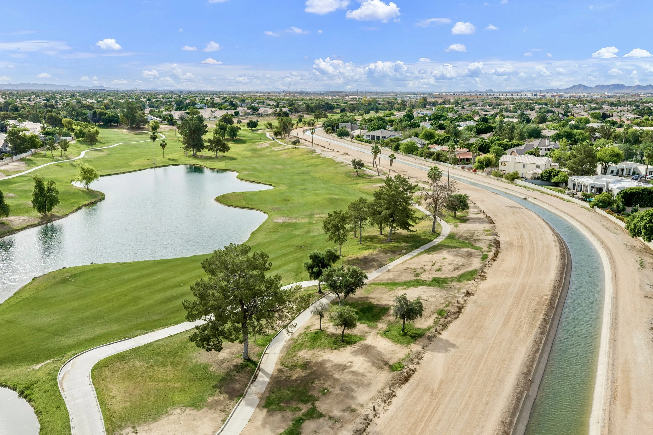 Aerial real estate photography showcasing a golf course, lake, and nearby homes in Gilbert, AZ, highlighting serene green spaces and water features in the neighborhood.