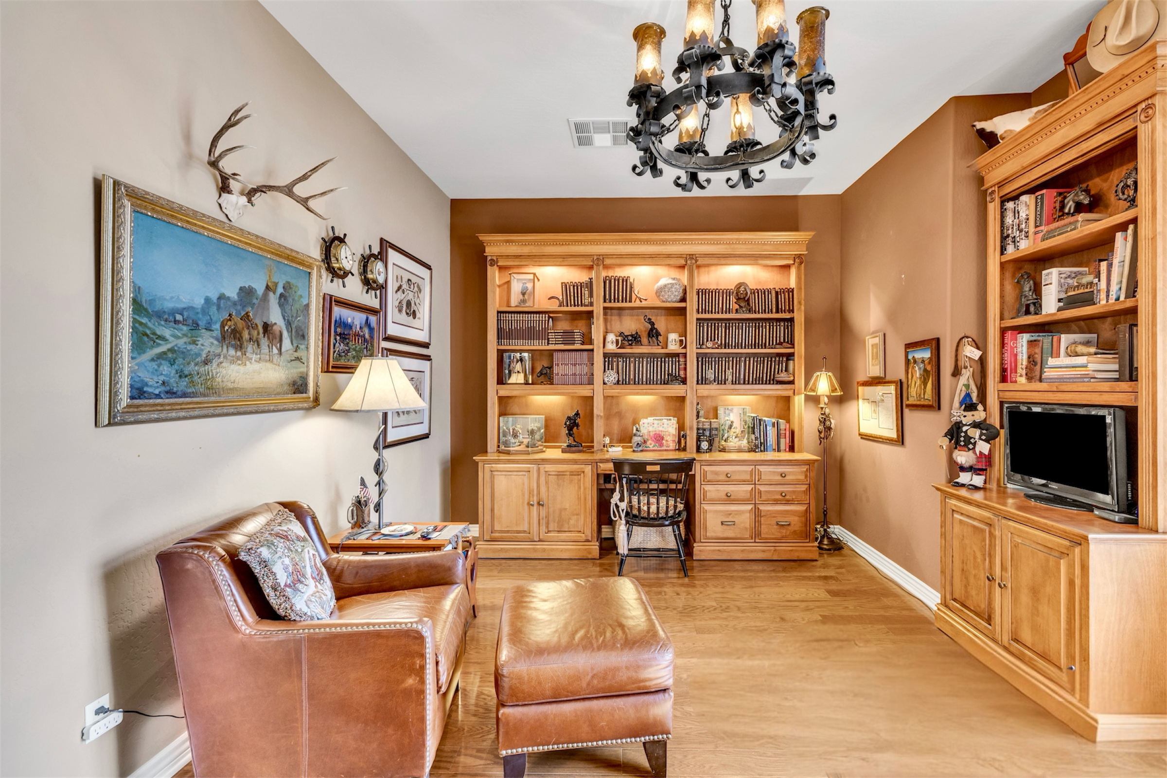 This cozy study room in Scottsdale, AZ features a leather chair, built-in wooden bookshelves, and warm lighting, showcasing excellent real estate photography for comfortable living spaces.
