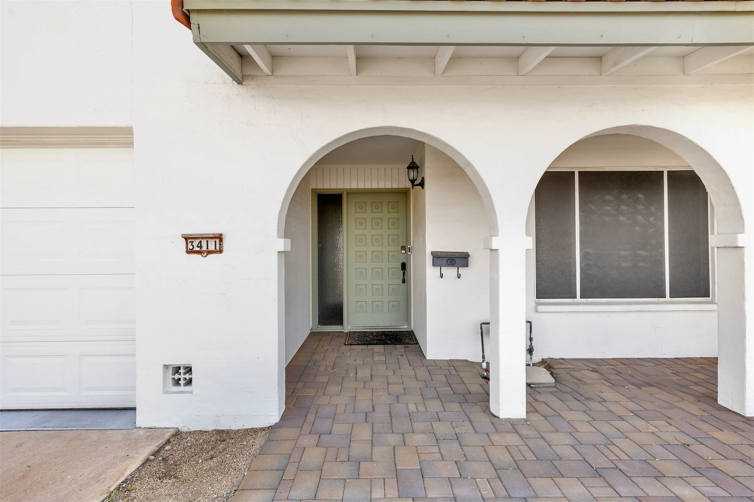 This image features a white arched entryway with a green door, showcasing charming architecture in Tempe, AZ, ideal for real estate photography highlighting residential curb appeal.
