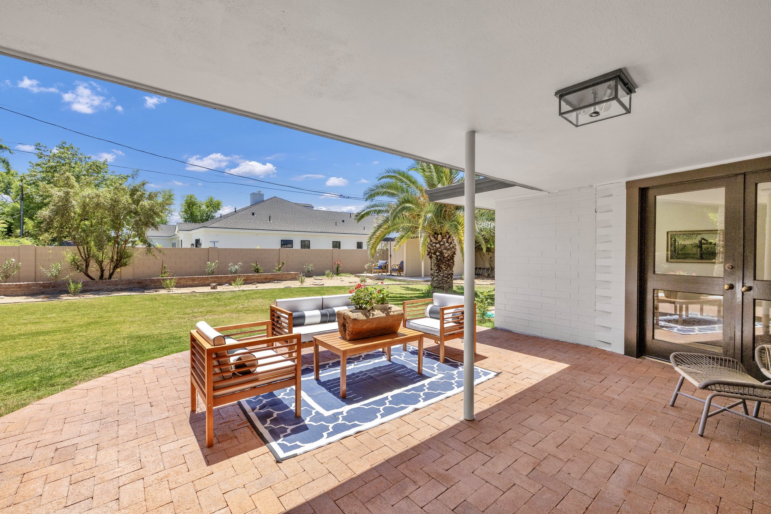 This covered patio with stylish wooden seating overlooks a lush backyard in Phoenix, AZ, showcasing excellent real estate photography that highlights outdoor living spaces.