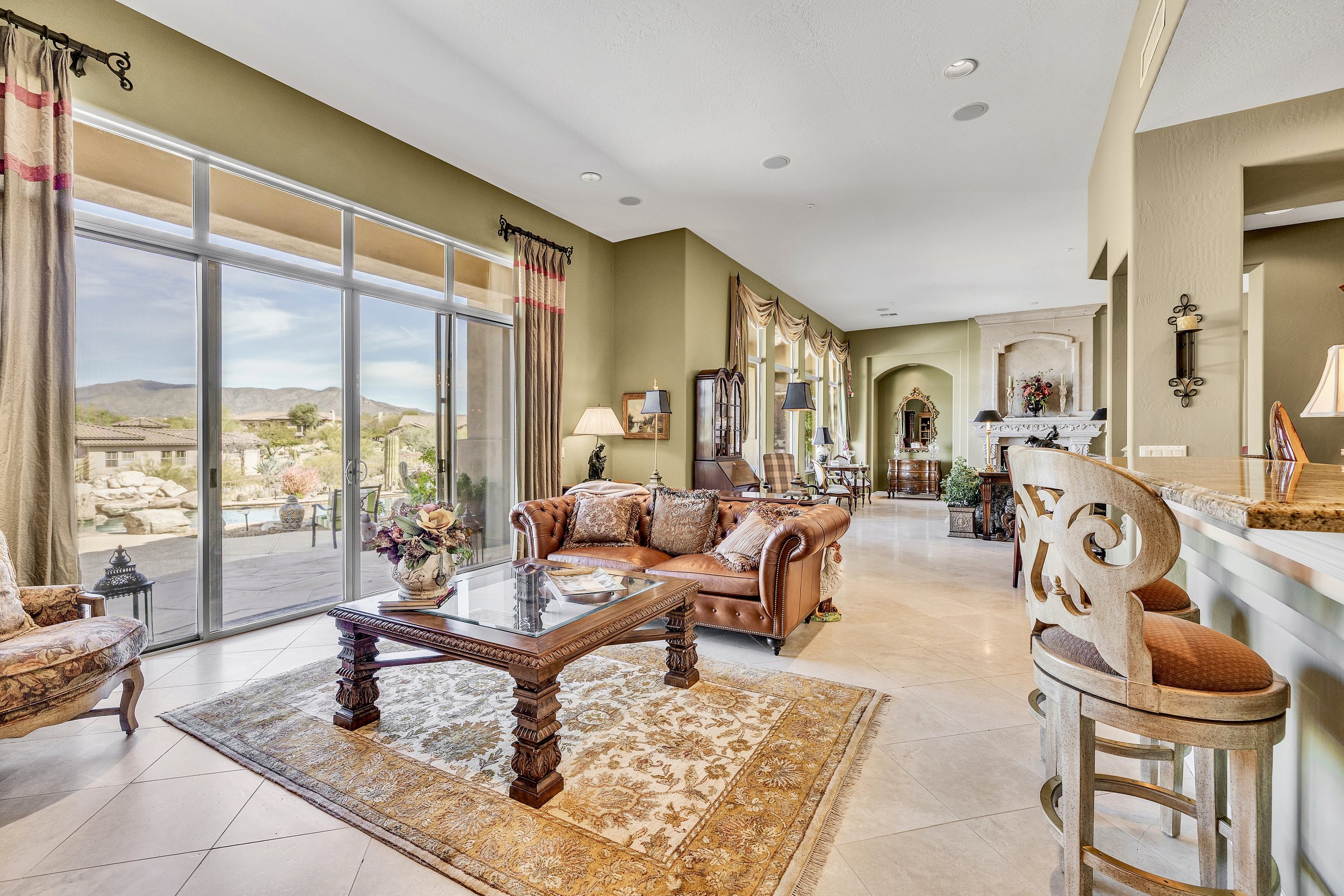 This spacious Scottsdale, AZ living room features large windows with patio and mountain views, showcasing elegant furnishings and high ceilings, captured with professional real estate photography.