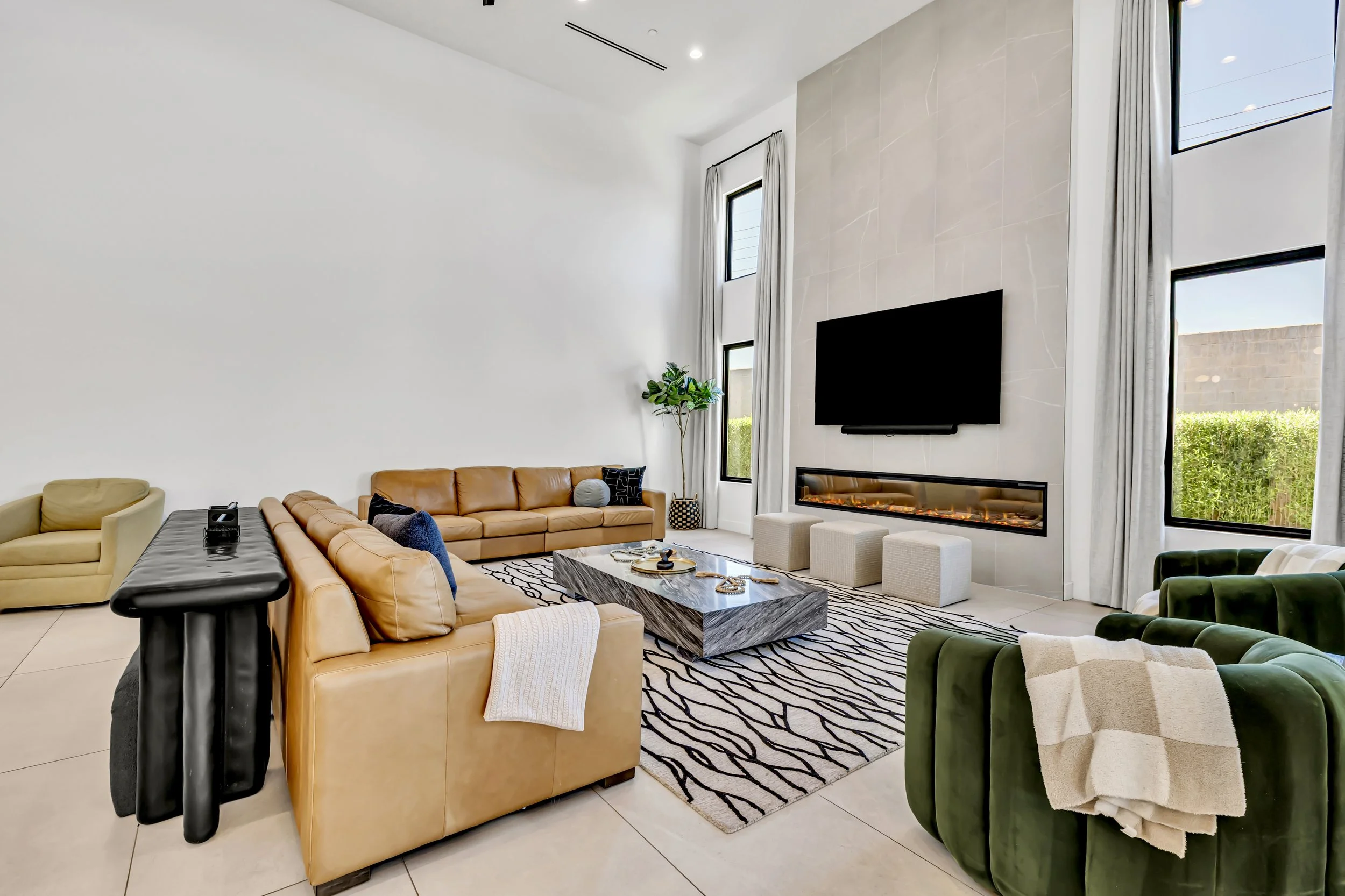 Spacious living room with multiple seating areas, a modern fireplace, tall windows, and sliding glass doors opening to the backyard in Scottsdale, Arizona.