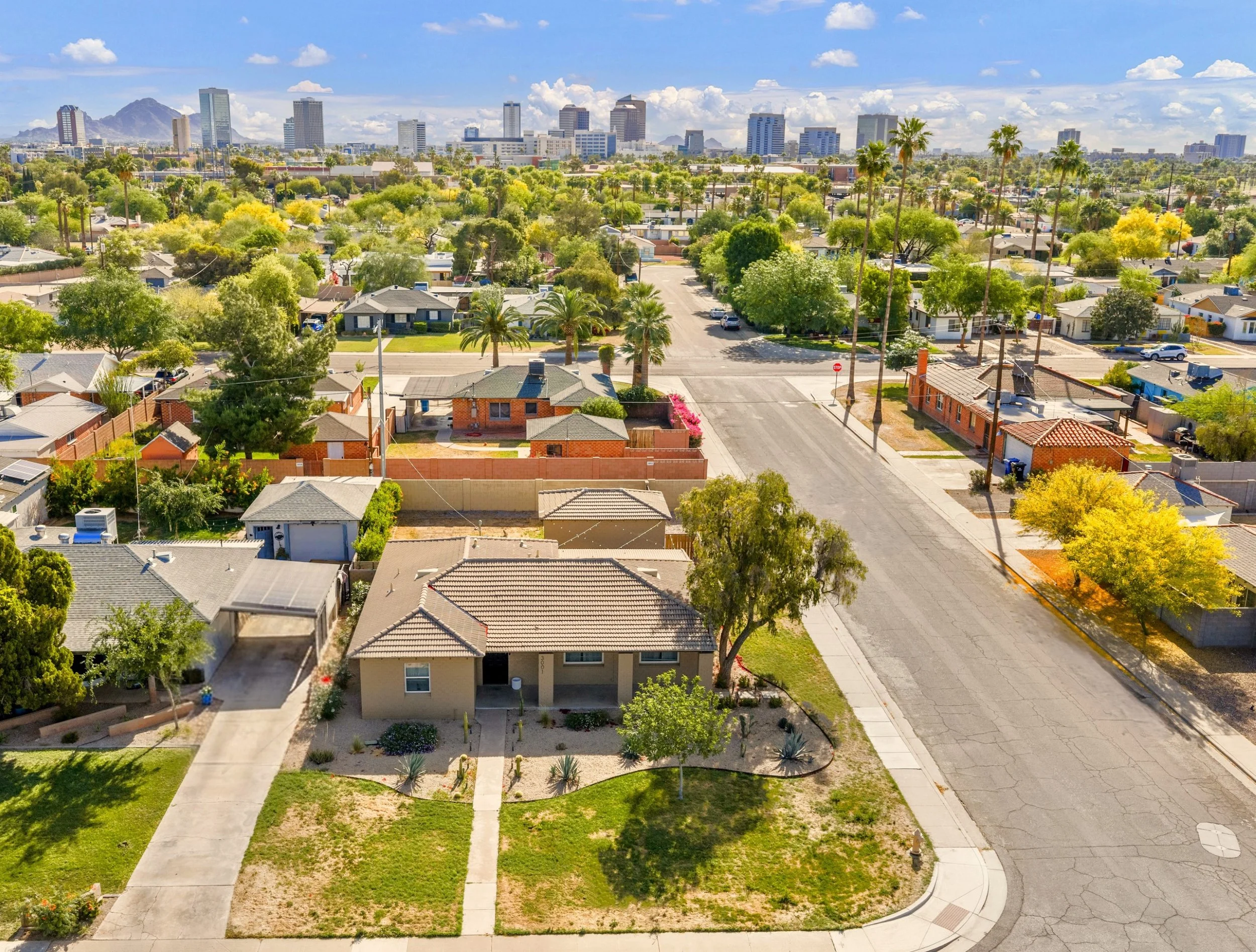 Aerial real estate photography showcasing a residential neighborhood in Phoenix, AZ with a clear city skyline backdrop and lush greenery surrounding the homes.