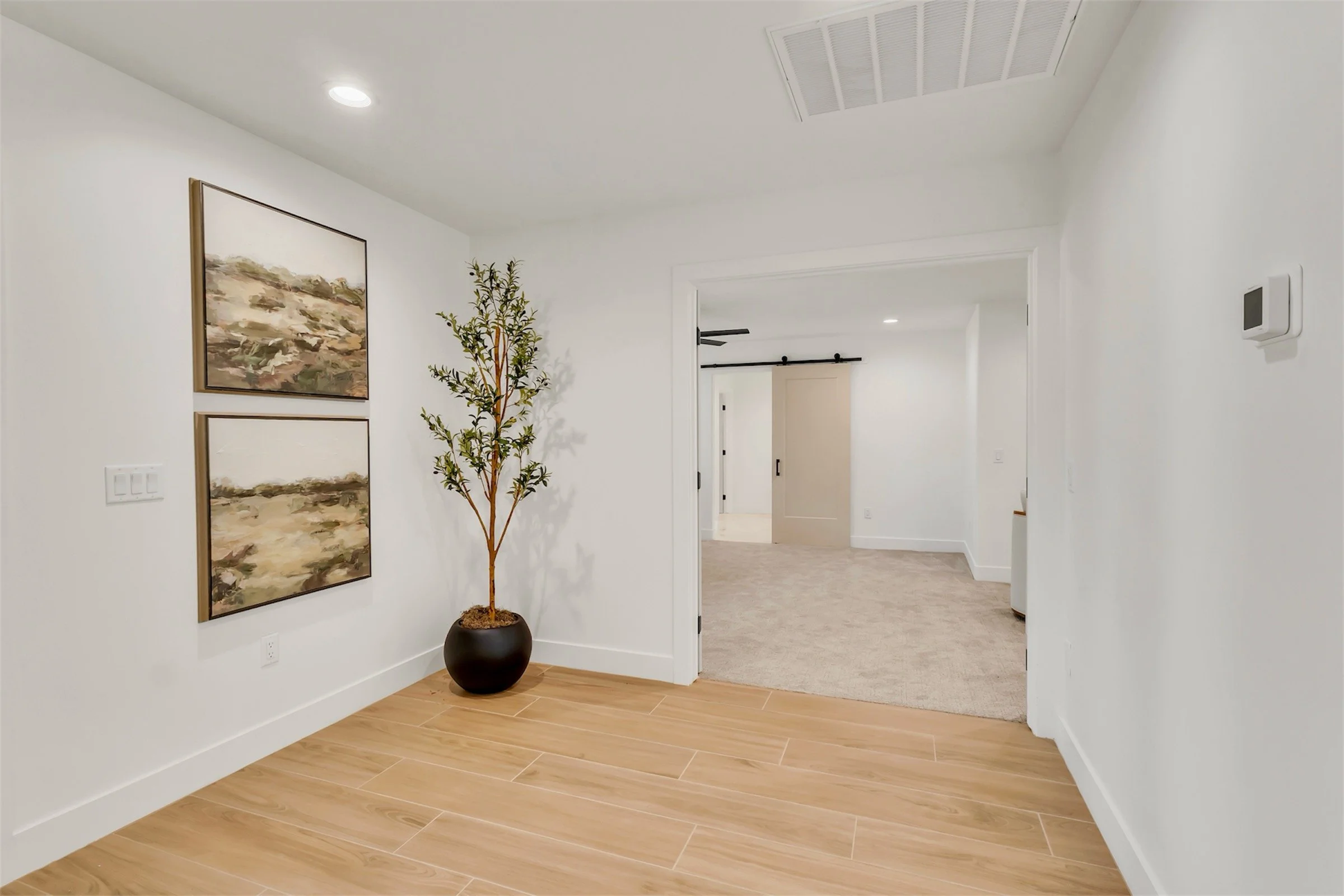Hallway in Phoenix, AZ home featuring wood-look tile flooring, modern decor, and a view toward the primary suite with barn door entry.