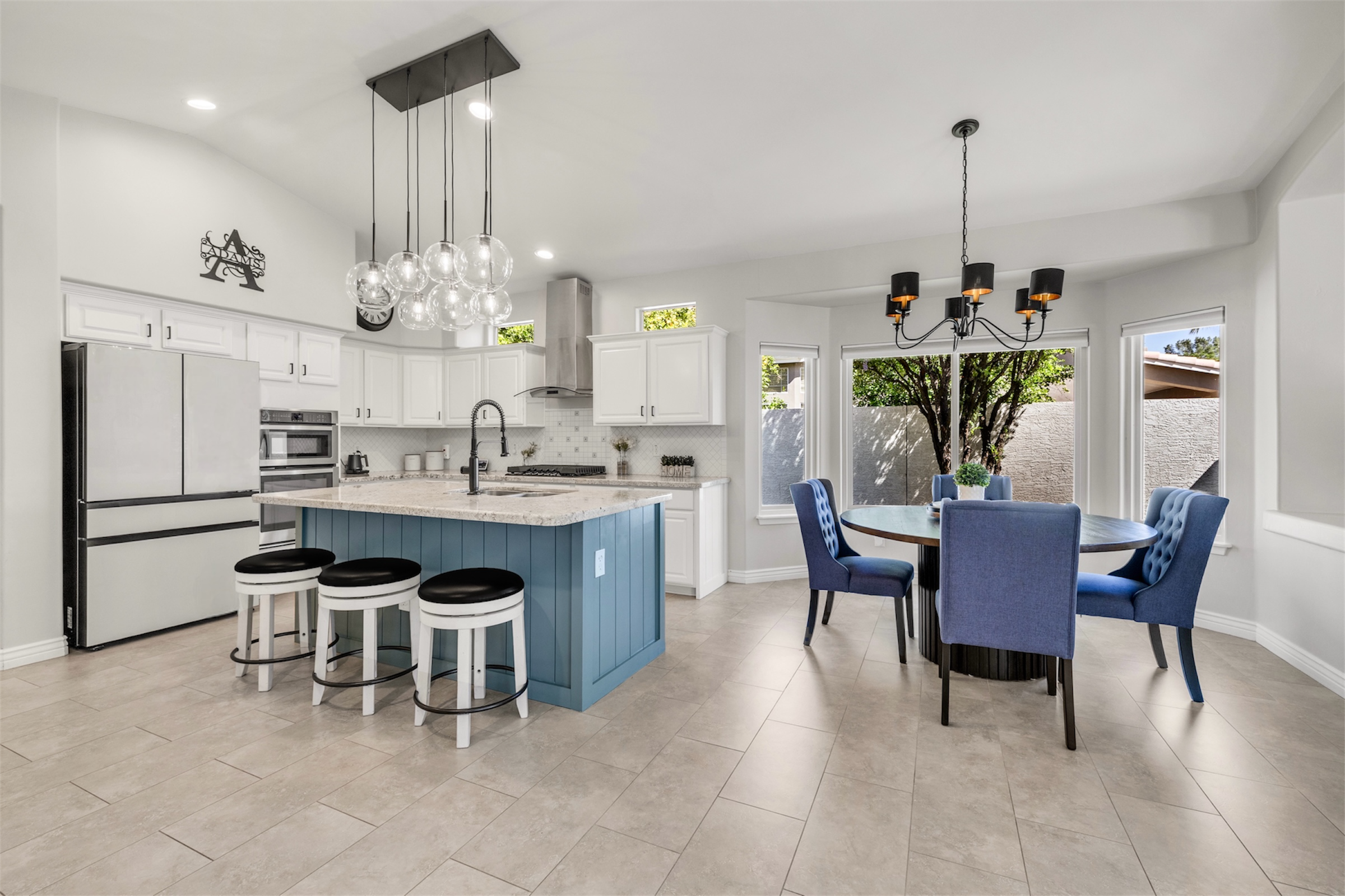 This bright kitchen with island and adjacent dining area features modern fixtures and large windows in a Gilbert, AZ home, ideal for real estate photography showcasing spacious and stylish interiors.