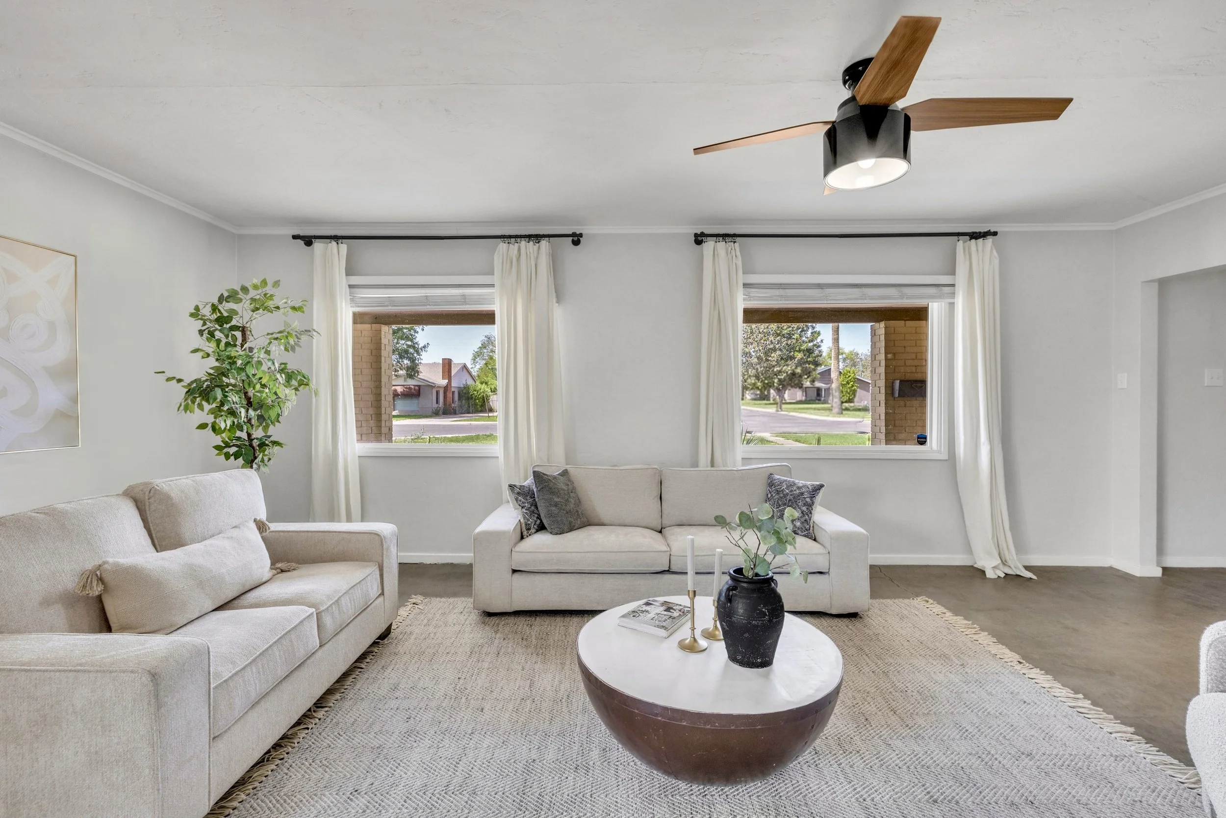 Bright and spacious living room with neutral sofas and a modern ceiling fan in Phoenix, AZ, captured through professional real estate photography.