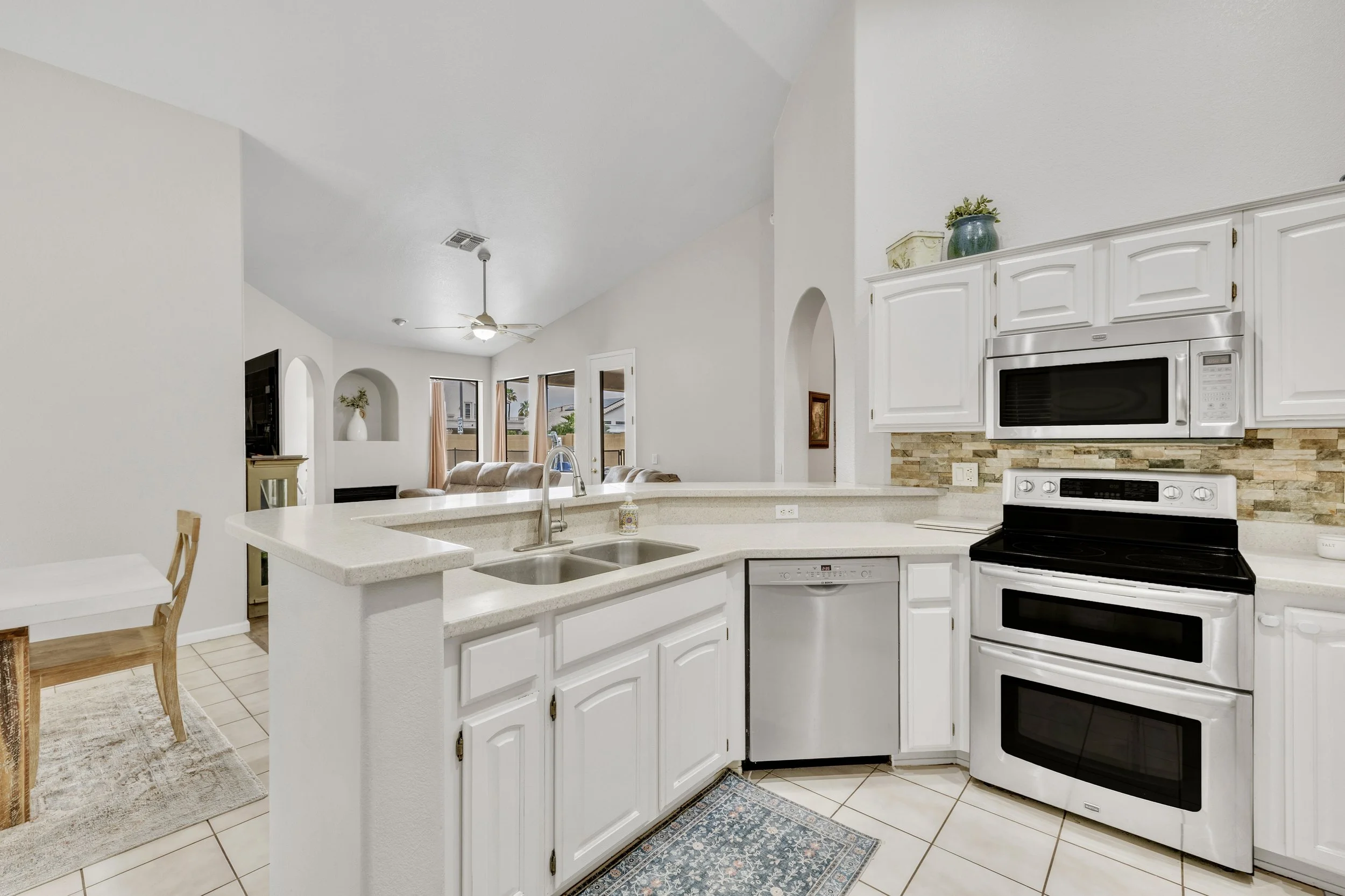 This bright kitchen with white cabinetry and modern appliances showcases open floor plan living in Goodyear, AZ, highlighting excellent real estate photography for potential buyers.