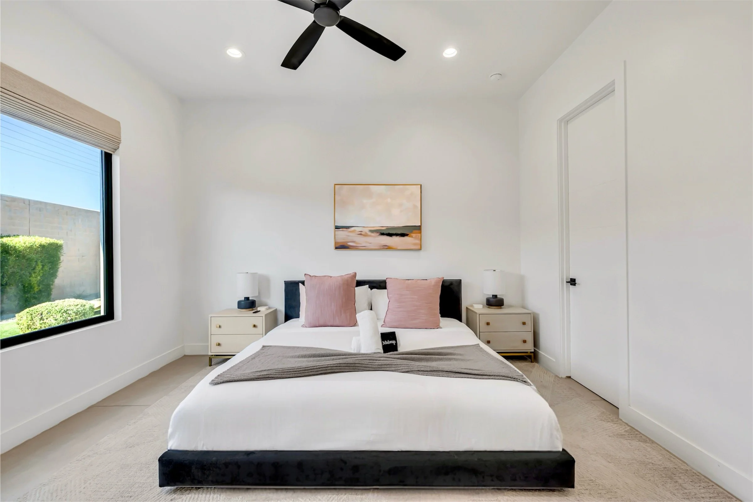 Minimalist bedroom with pink accent pillows, modern nightstands, and a large window in Scottsdale, Arizona.