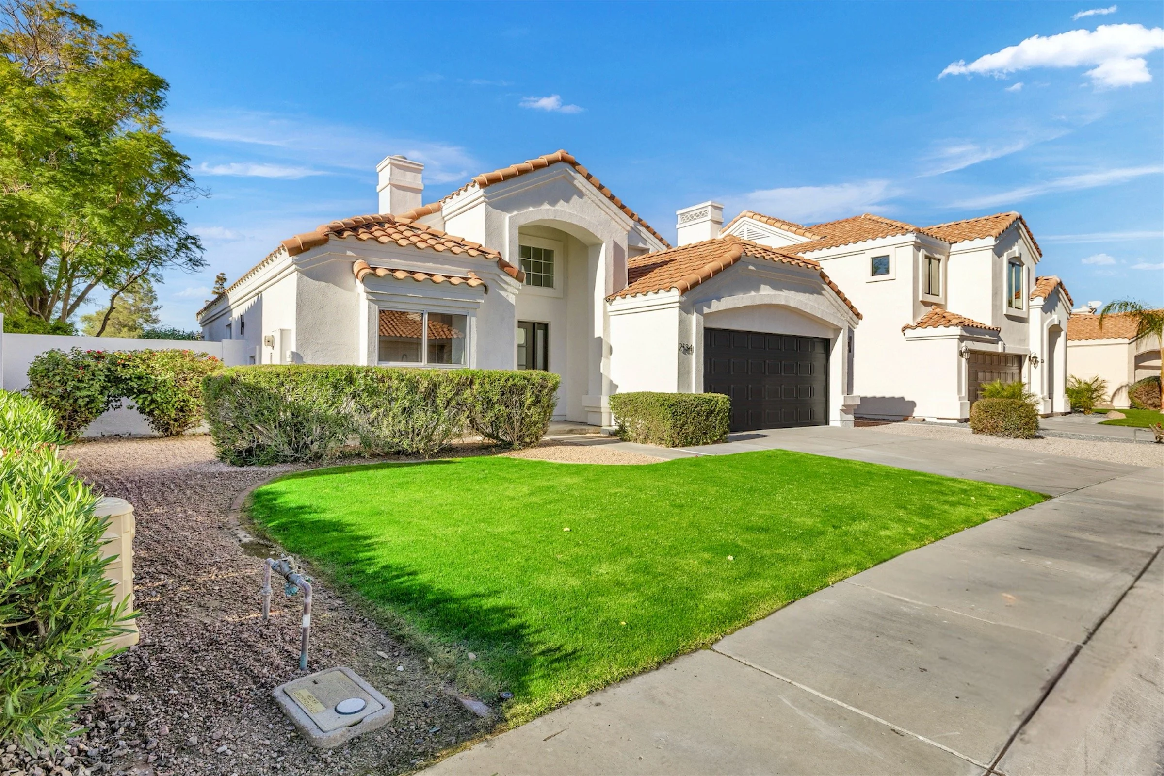 Stunning real estate photography of a modern home with a manicured lawn and tiled roof in Chandler, AZ on W Peninsula Cir, showcasing beautiful curb appeal and sunny skies.