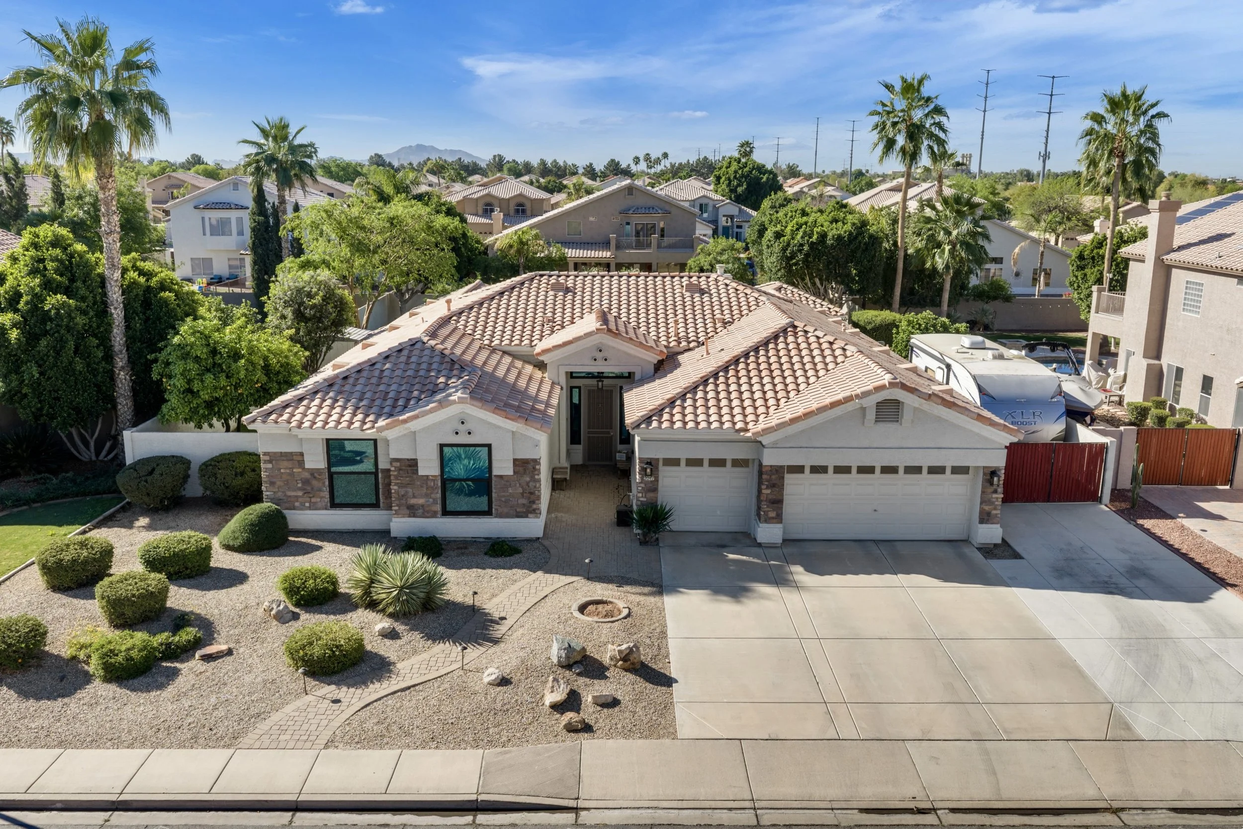 Aerial real estate photography shows a spacious suburban home with desert landscaping in Gilbert, AZ, featuring a three-car garage and tile roof.