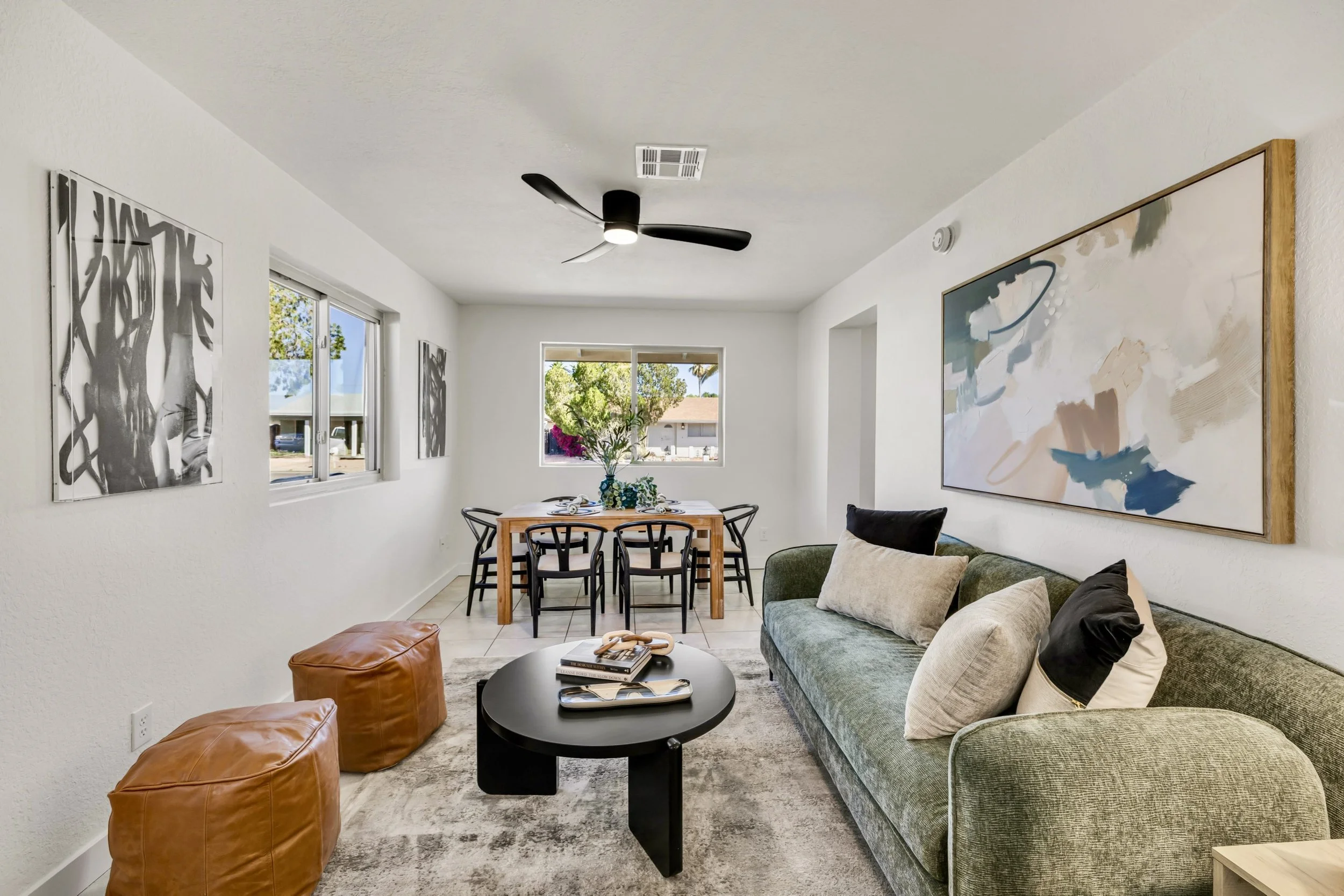 Bright modern living room and dining area with stylish decor shown in real estate photography in Mesa, AZ, highlighting a cozy green sofa, a black coffee table, and natural light through large windows.
