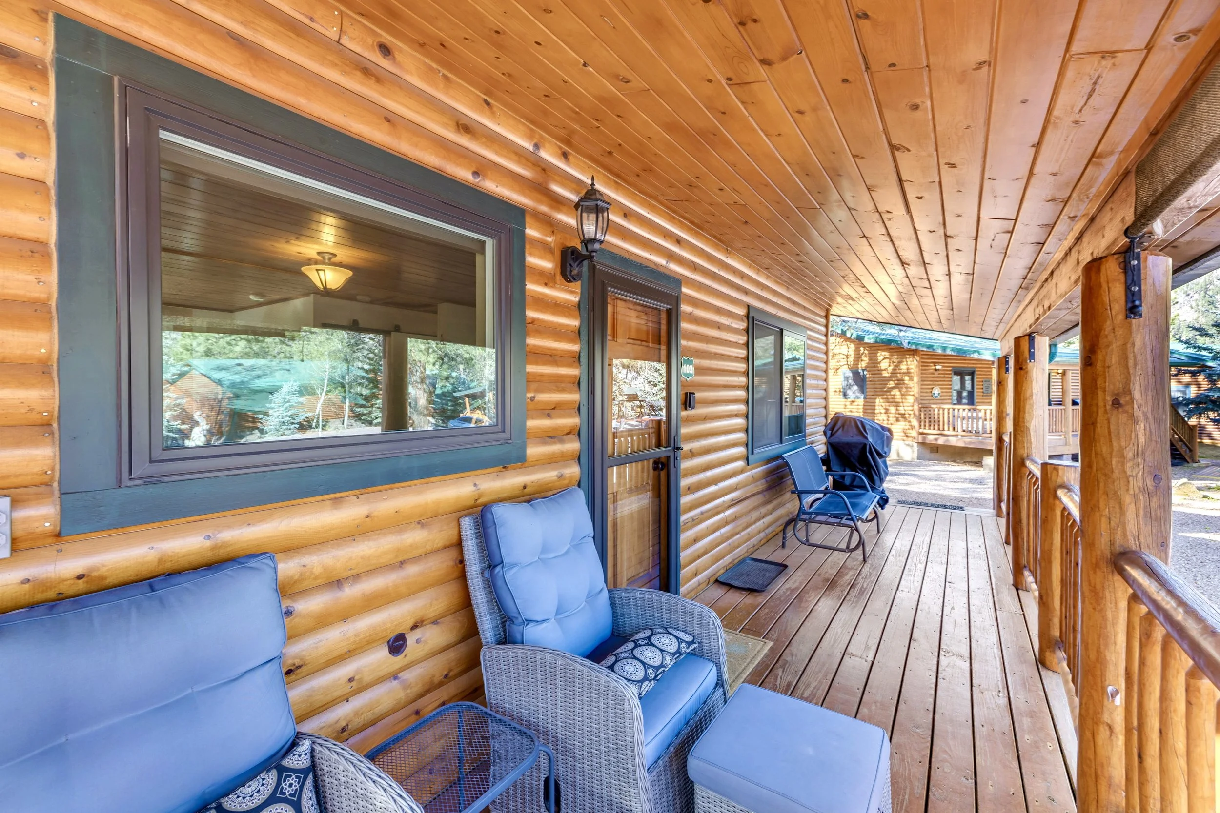 This inviting wooden cabin porch with comfortable outdoor seating exemplifies rustic charm in Greer, AZ, captured with expert real estate photography to highlight its cozy appeal.