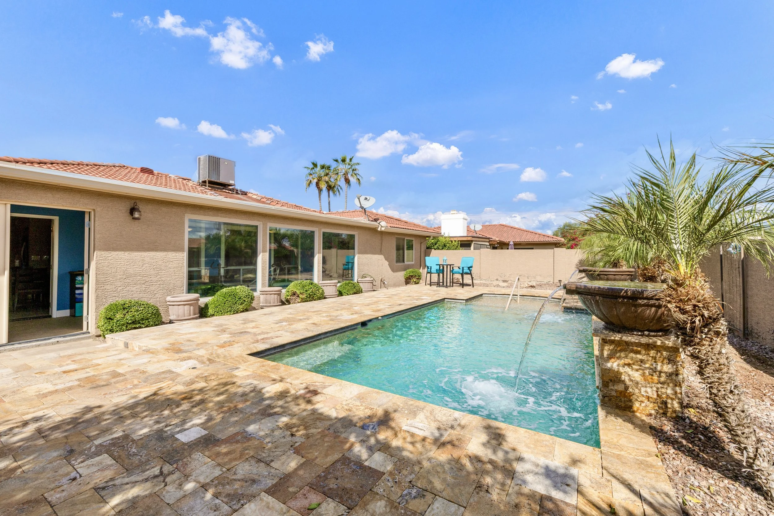 This Sun Lakes, AZ backyard features a sparkling swimming pool with a tiled deck and palm trees, captured beautifully in real estate photography showcasing outdoor living space.