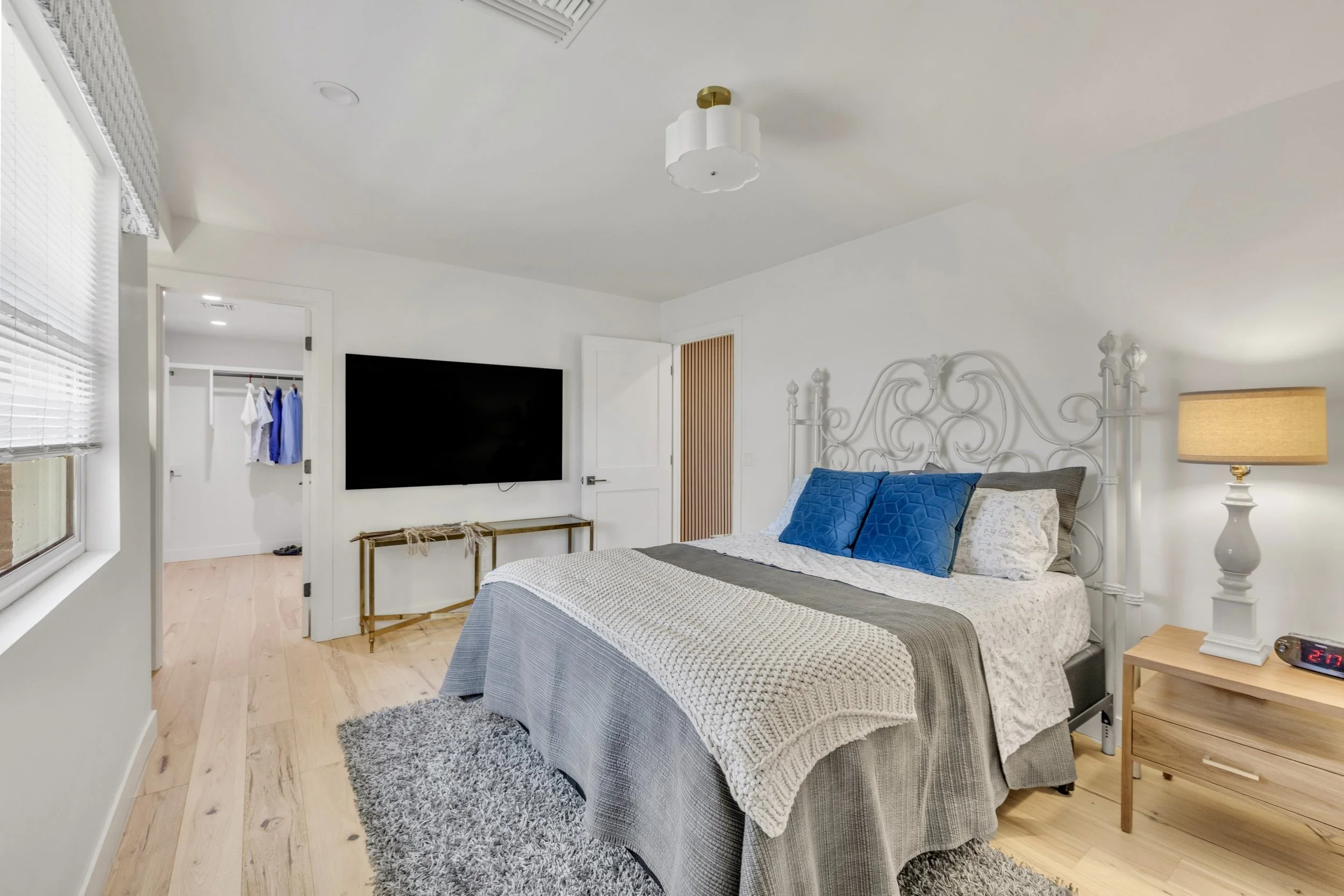 This bright and cozy bedroom in Phoenix, AZ features a gray bed with blue pillows, wooden flooring, and modern decor, perfect for real estate photography showcasing comfortable living spaces.