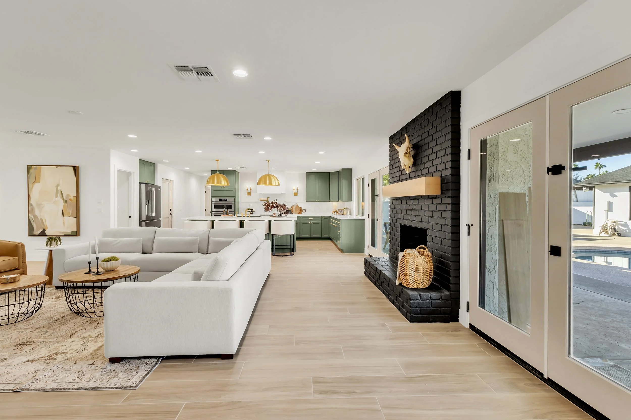 Modern living room in Phoenix, AZ featuring green kitchen cabinetry, black fireplace, and large white sectional.