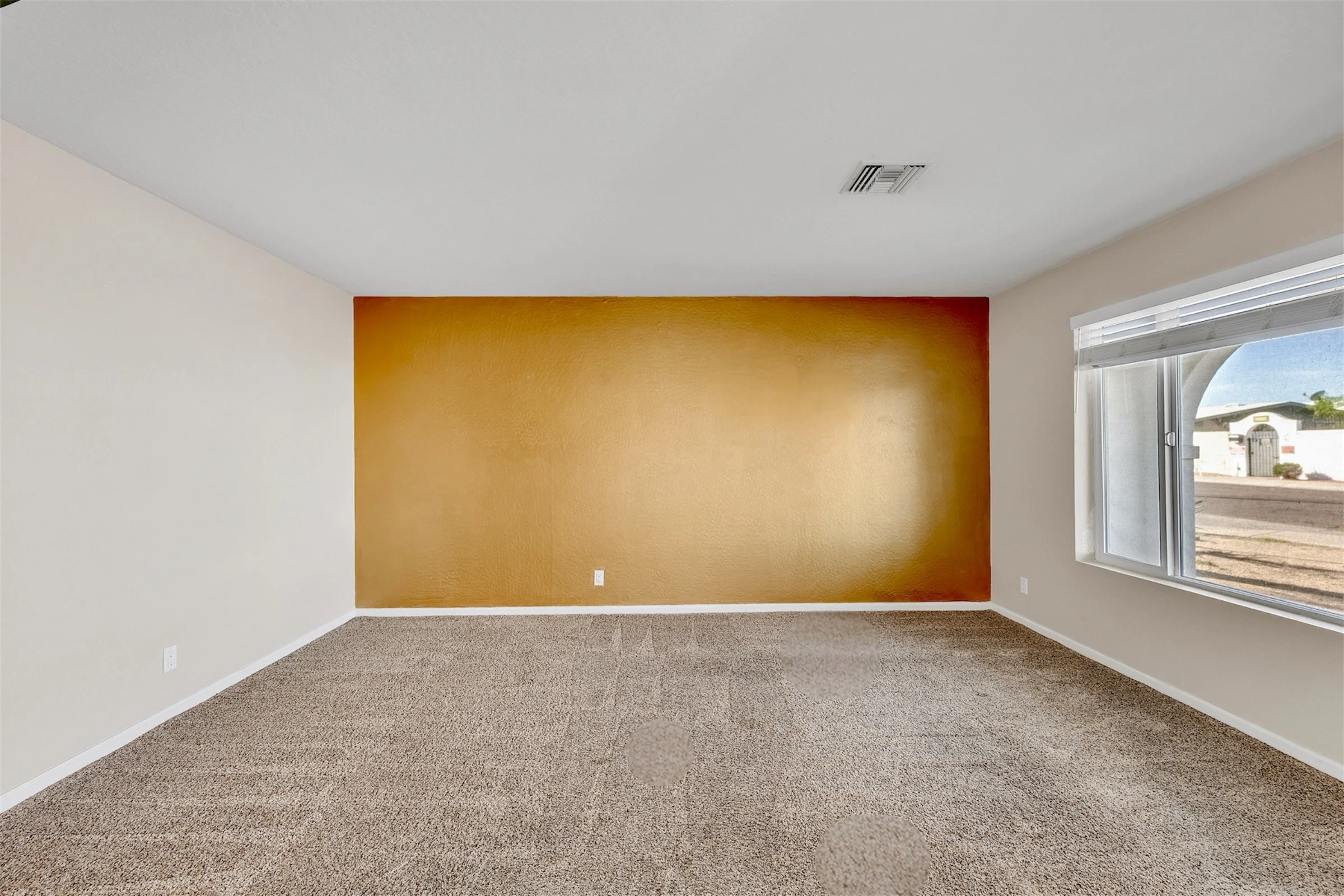 This empty room in Tempe, AZ features an ochre accent wall and ample natural light, perfect for showcasing real estate photography in the area.