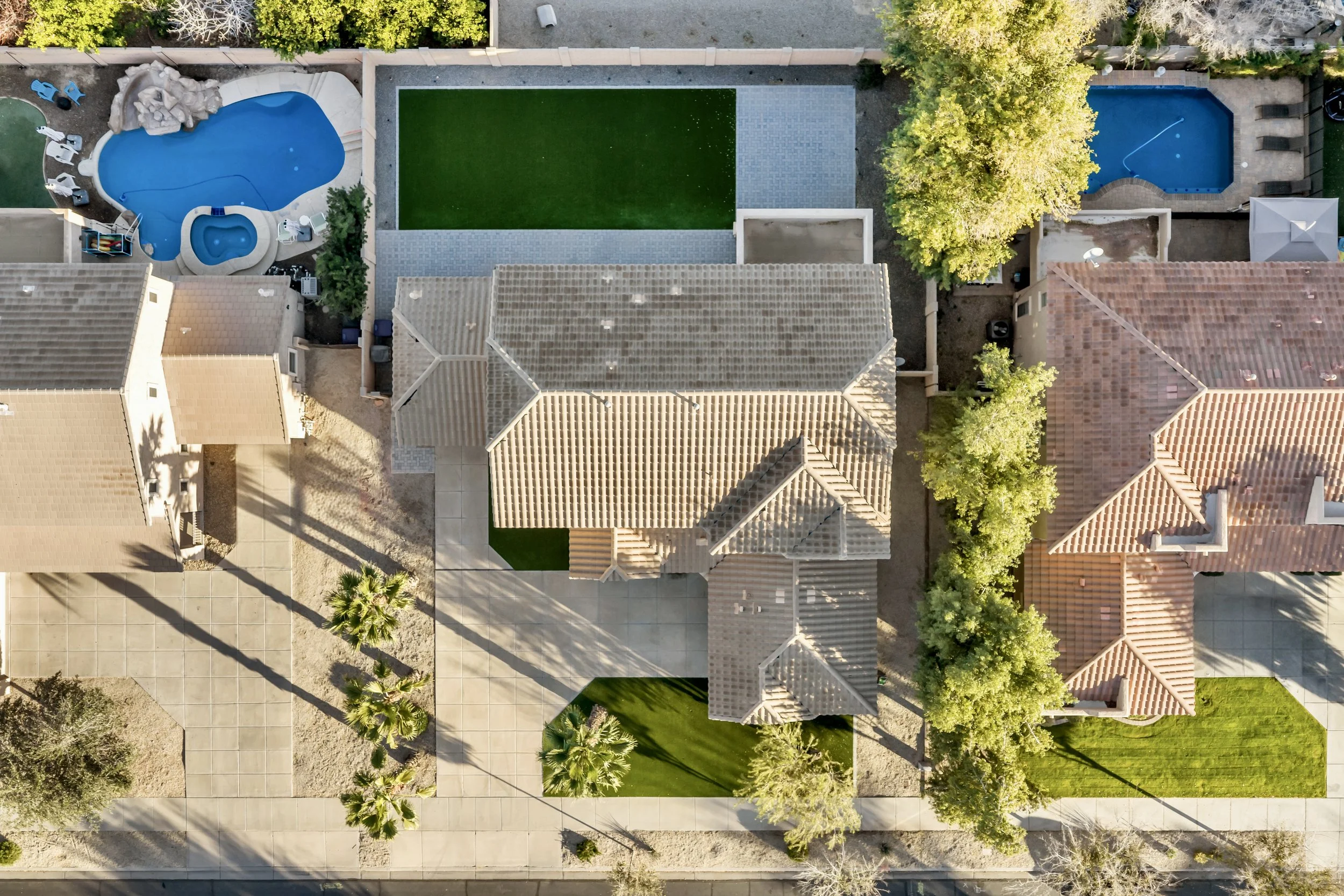 Aerial view of residential homes with swimming pools and well-maintained yards in Queen Creek, AZ, showcasing a beautiful neighborhood with desert landscaping and rooftop details.