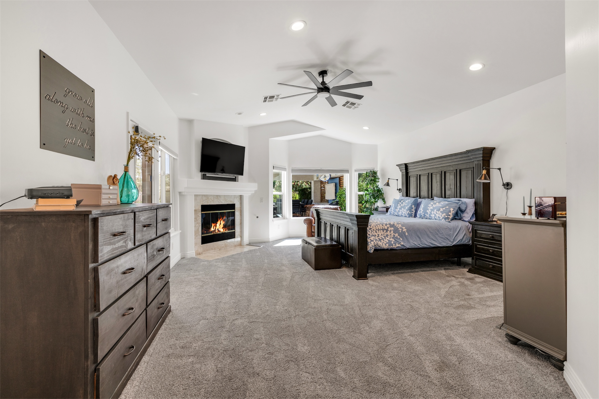 Spacious master bedroom in Gilbert, AZ with carpet flooring, a fireplace, and modern ceiling fan offers a cozy and elegant living space, highlighted by professional real estate photography.