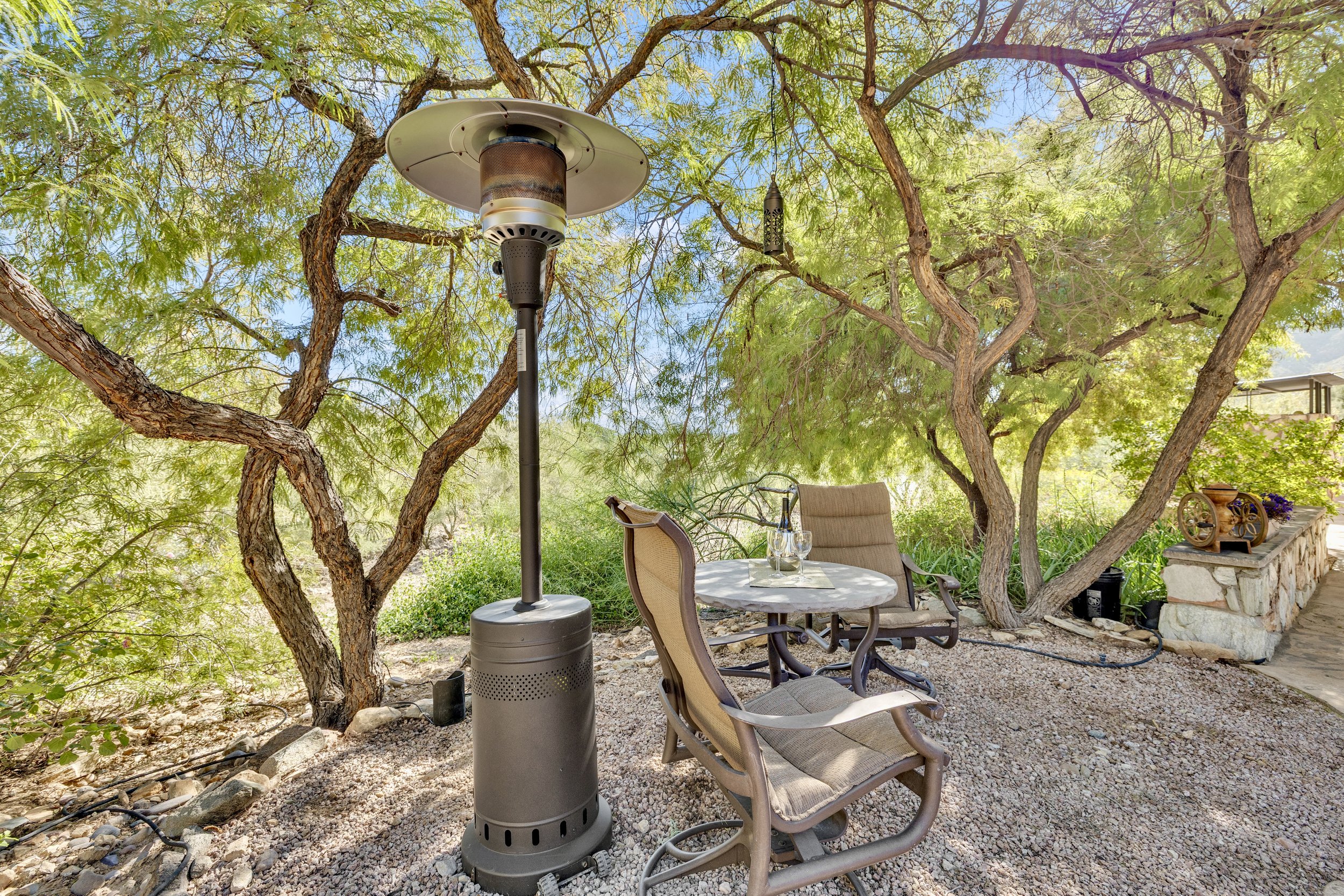 This shaded outdoor patio area in Paradise Valley, AZ offers a cozy seating arrangement with a patio heater, perfect for enjoying nature in comfort. Real estate photography highlights this inviting space.