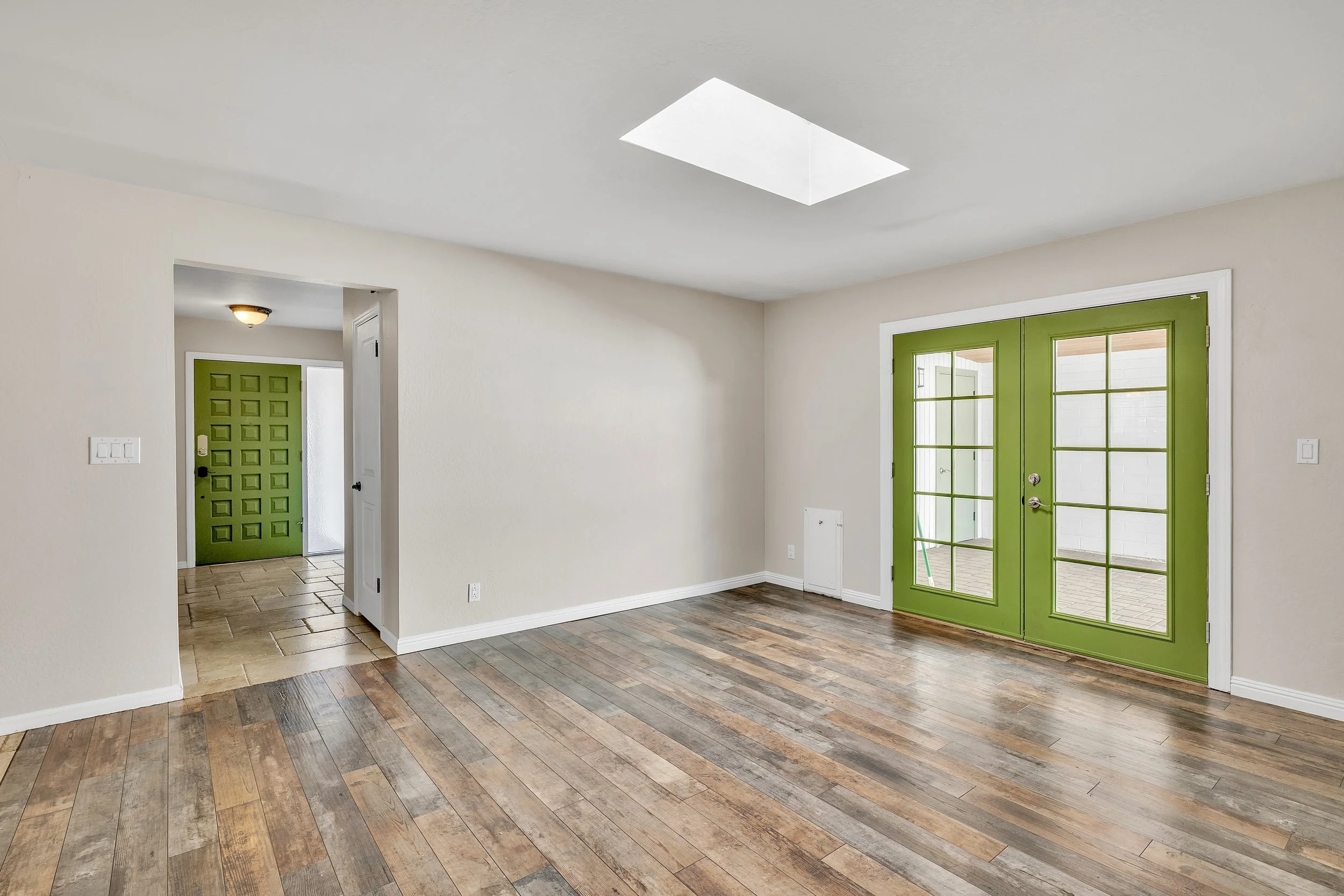 This bright empty living room features green French doors and a skylight, showcasing a stylish space in Tempe, AZ through high-quality real estate photography.