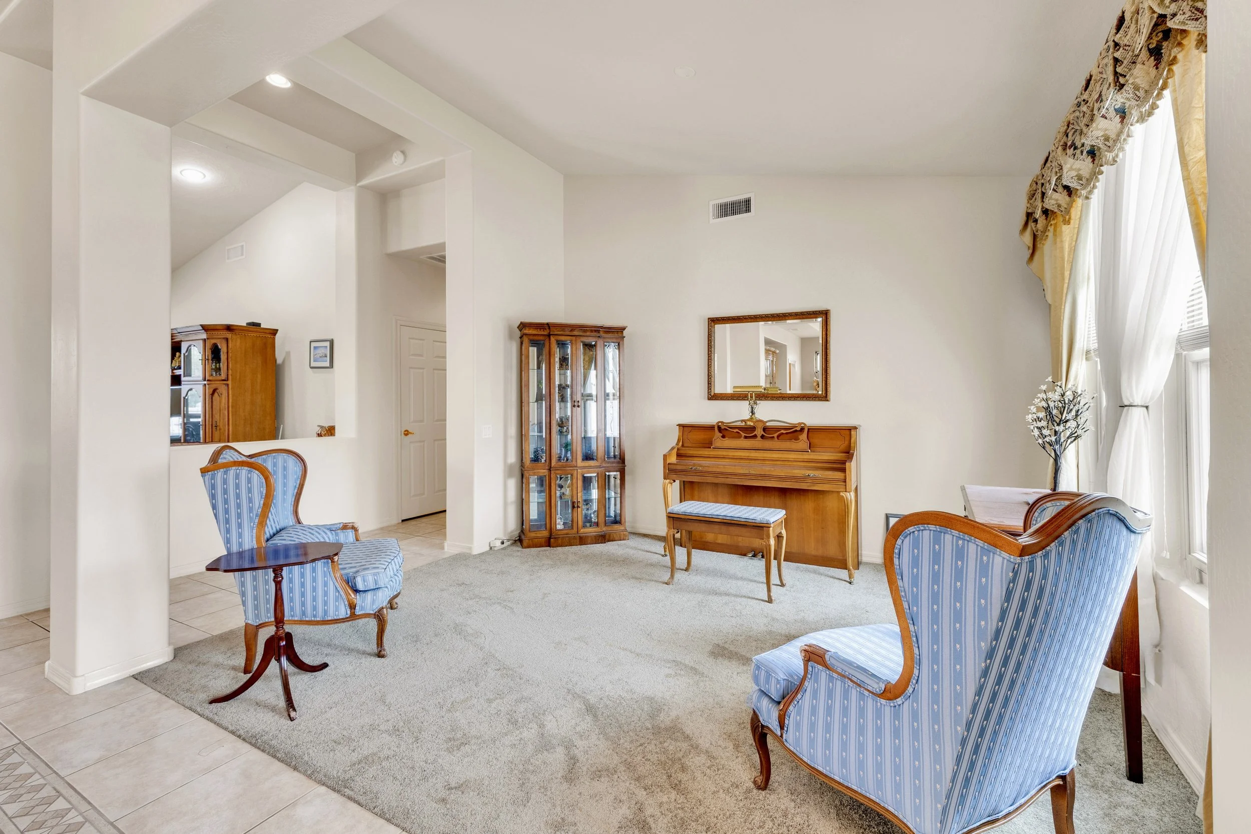 This bright living room with a piano and blue armchairs showcases elegant real estate photography in Surprise, AZ, highlighting a spacious and inviting home interior.