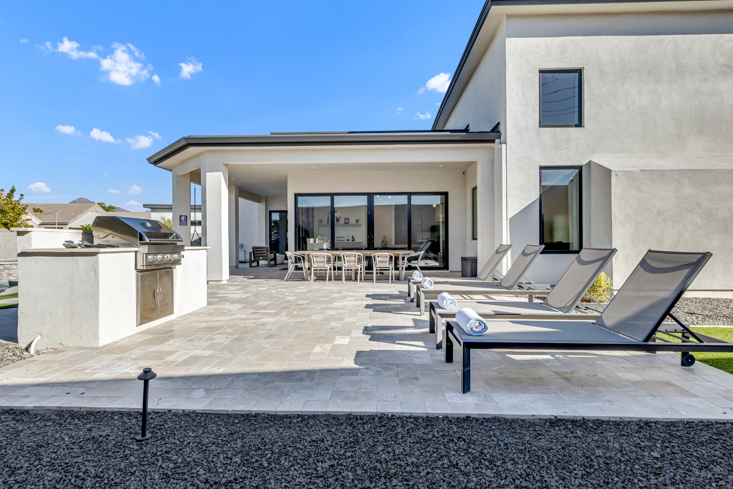Backyard patio with outdoor grill, dining table, and multiple lounge chairs for sunbathing in Scottsdale, Arizona.