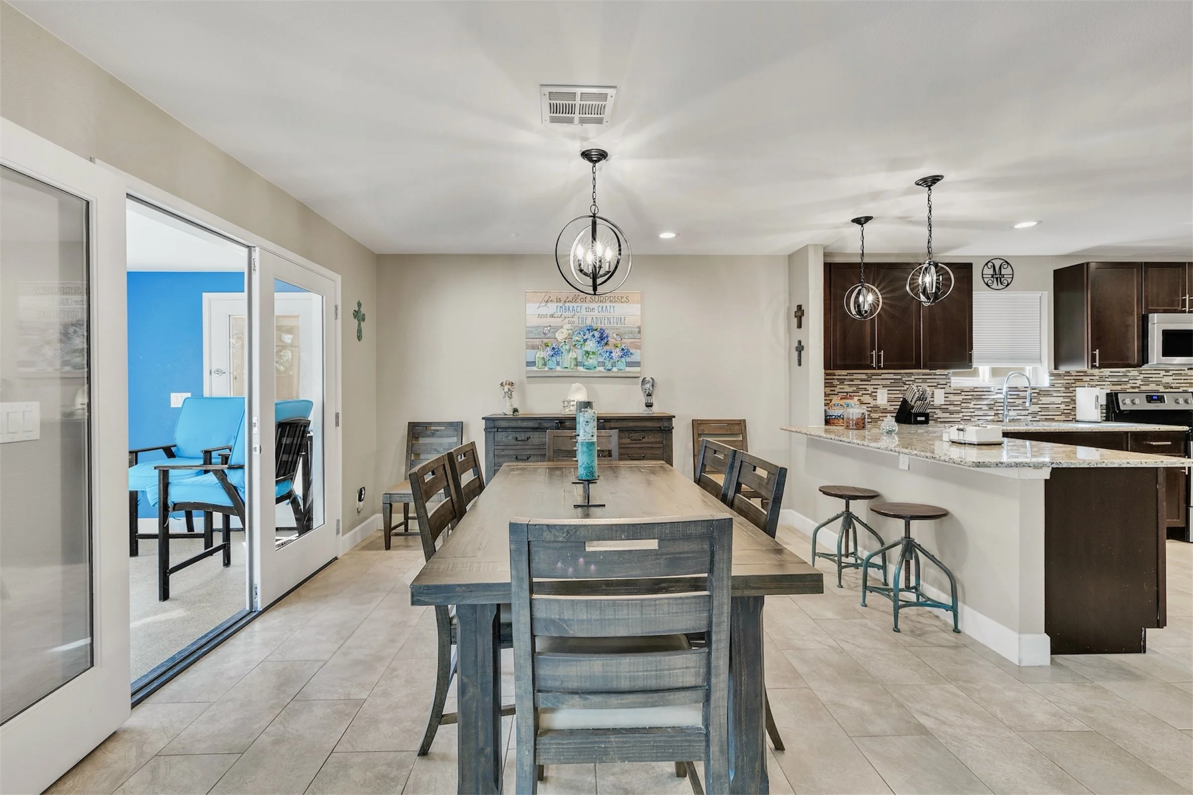 This Sun Lakes, AZ home features an open-concept dining room and kitchen with modern lighting and a bright adjacent room, captured beautifully in this real estate photography.