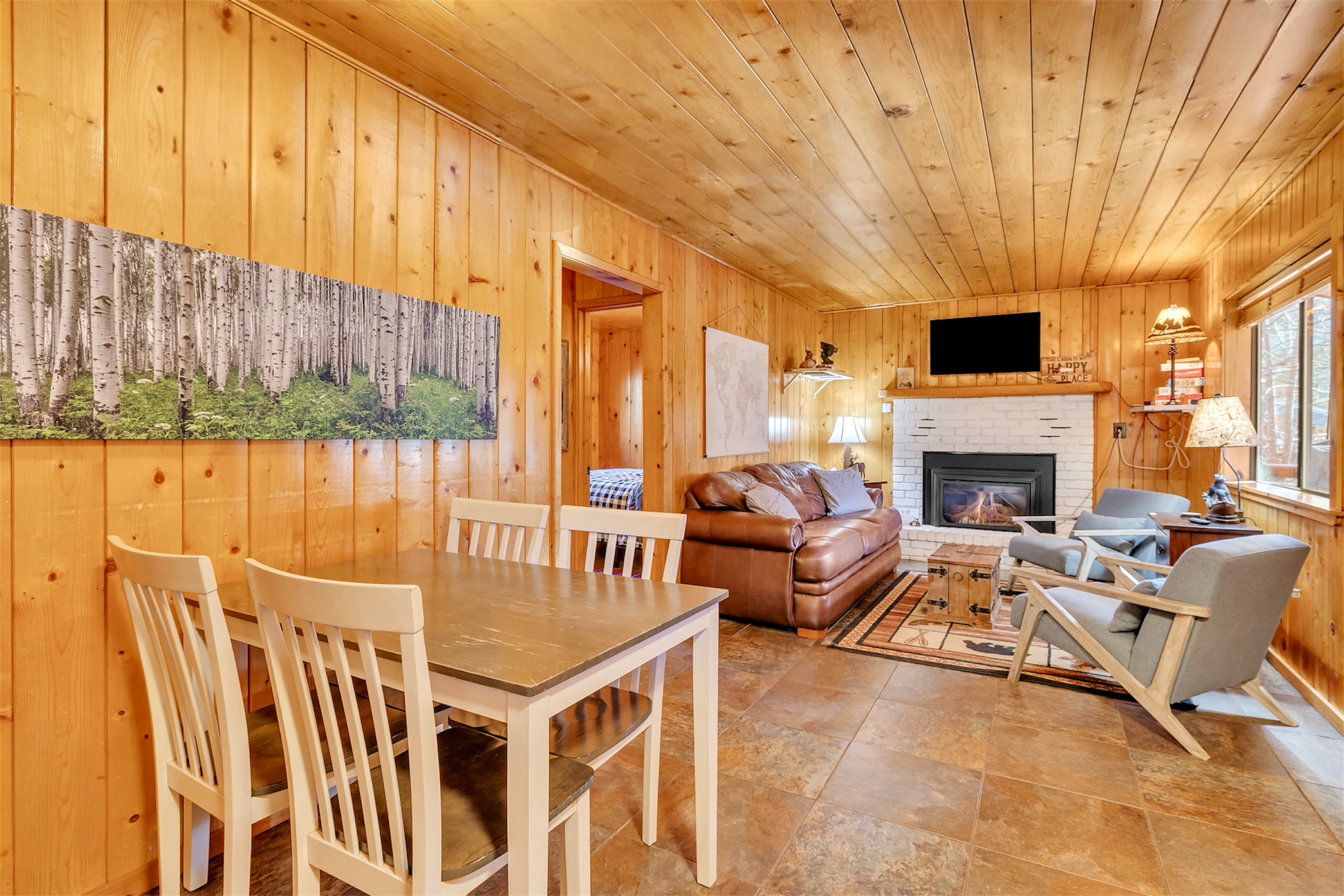 Cozy wood-paneled living room with fireplace and dining area showcases charming real estate photography in Greer, AZ.