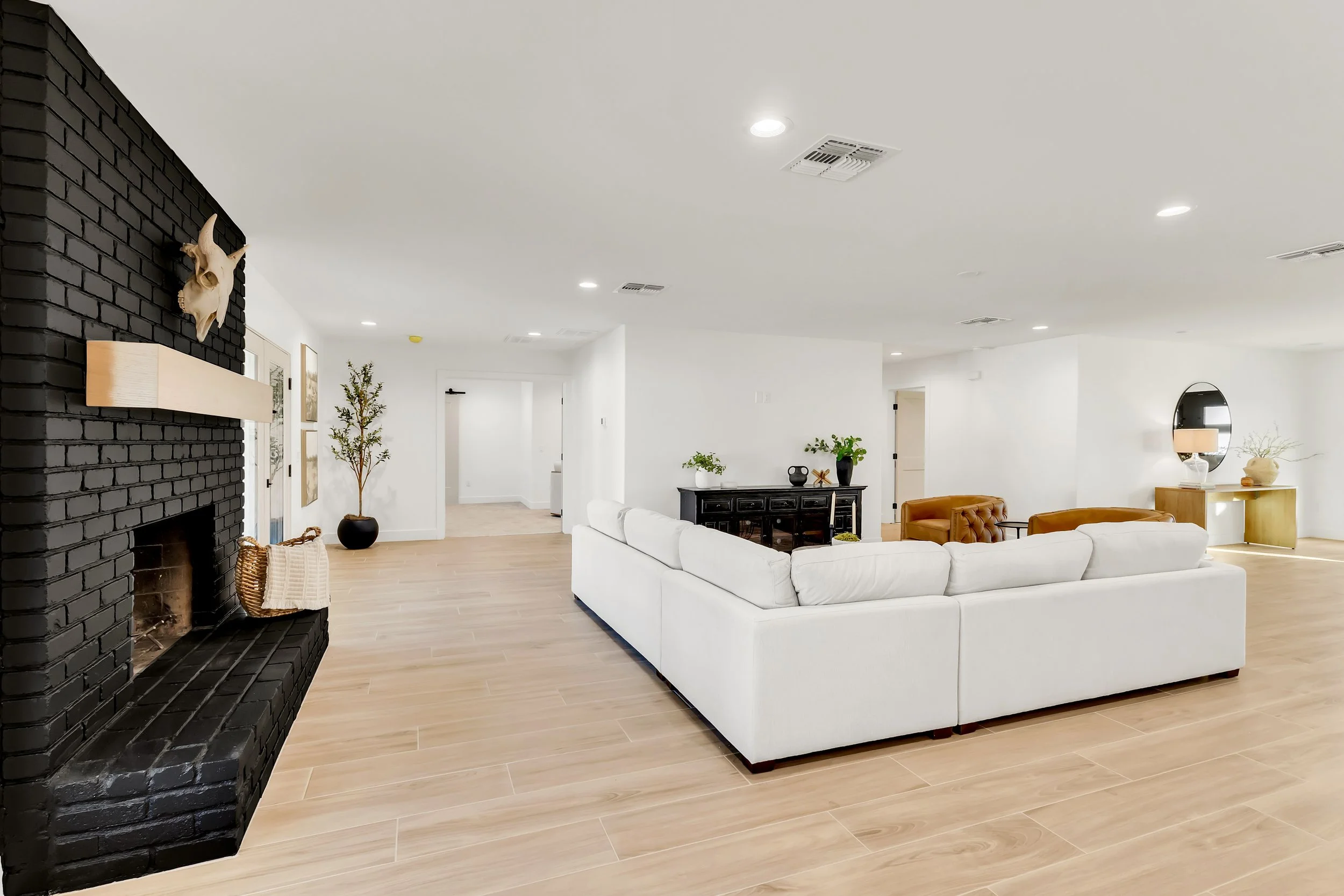 Open-concept living room in Phoenix, AZ showcasing a black brick fireplace, white sectional sofa, and light wood flooring.