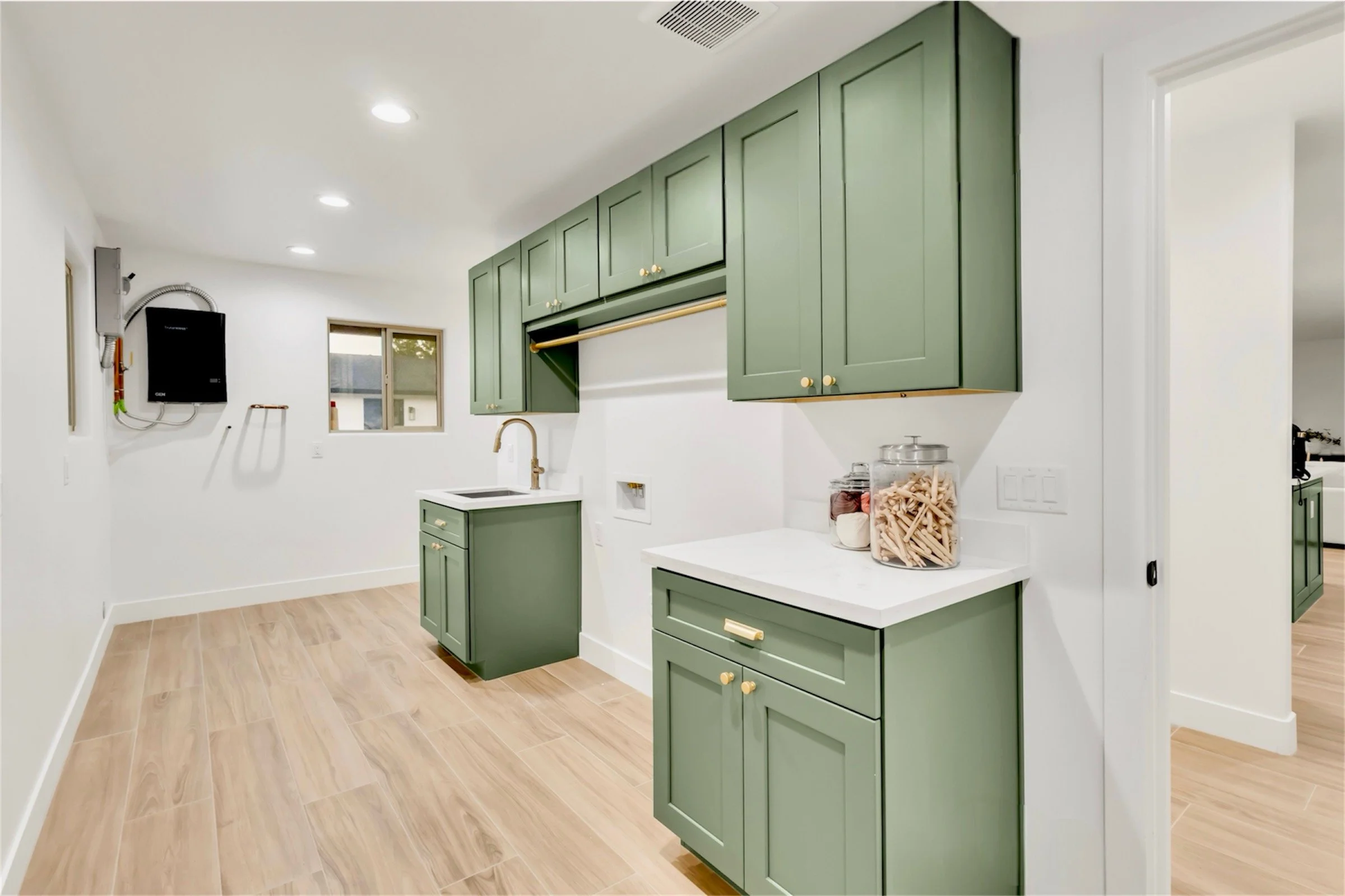 Stylish laundry room in Phoenix, AZ featuring green cabinetry, gold hardware, and modern wood-look tile flooring.