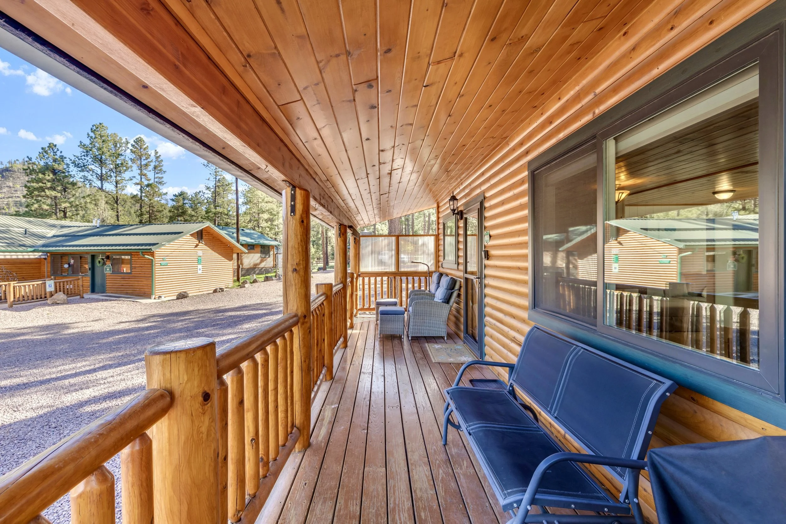 This real estate photography showcases a wooden covered porch with seating in Greer, AZ, highlighting the rustic charm and peaceful atmosphere of the property.