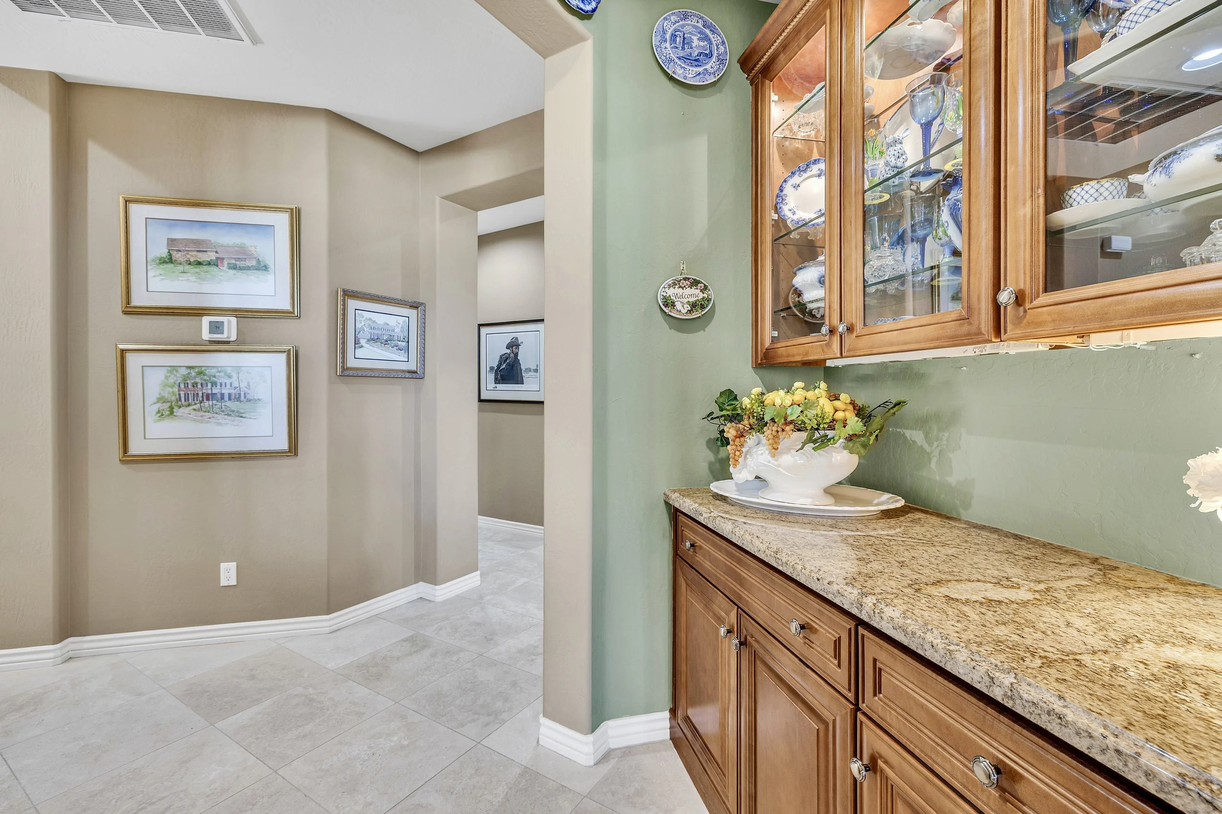 This Scottsdale, AZ home features a stylish kitchen cabinet with granite countertop and a hallway adorned with framed artwork, captured through expert real estate photography.