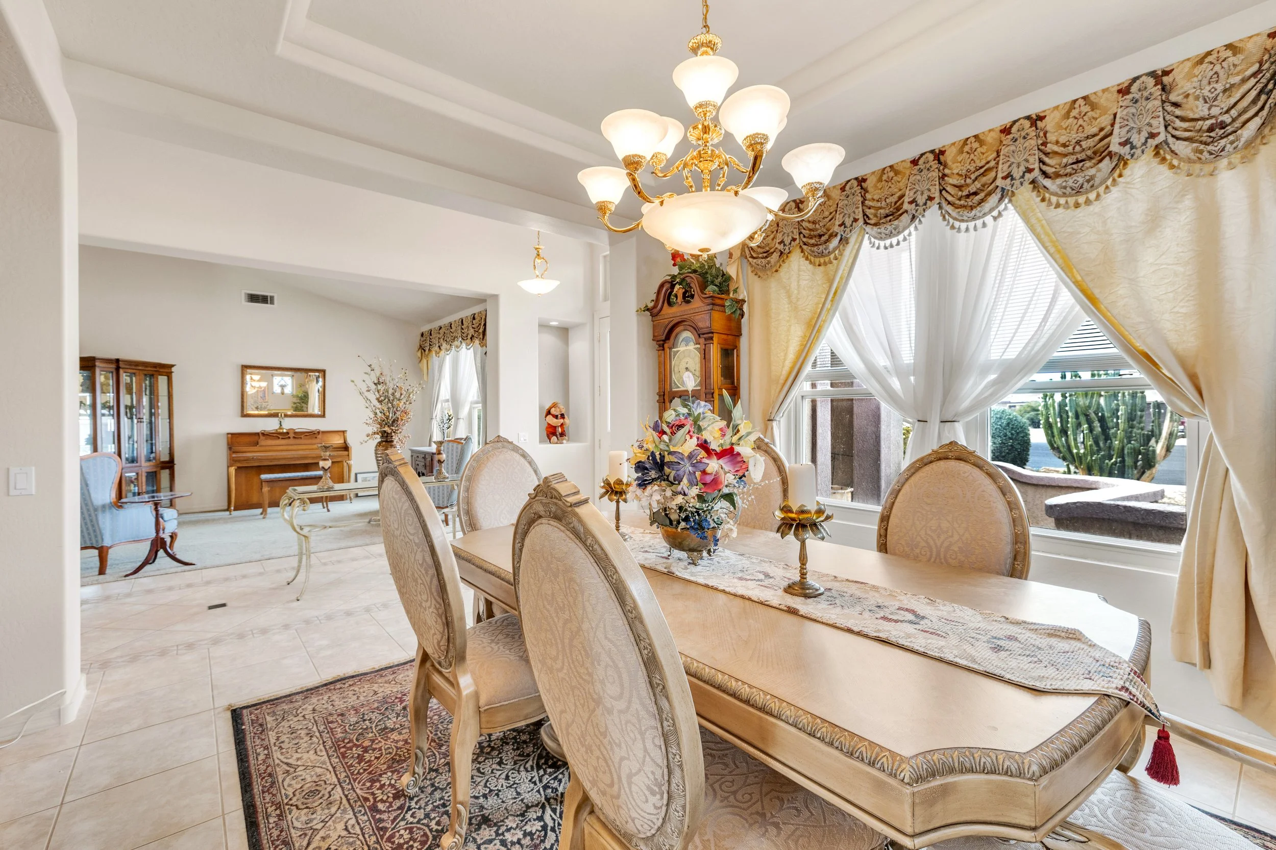 This elegant dining room in Surprise, AZ features a classic chandelier, ornate chairs, and large windows for natural light, captured through professional real estate photography.