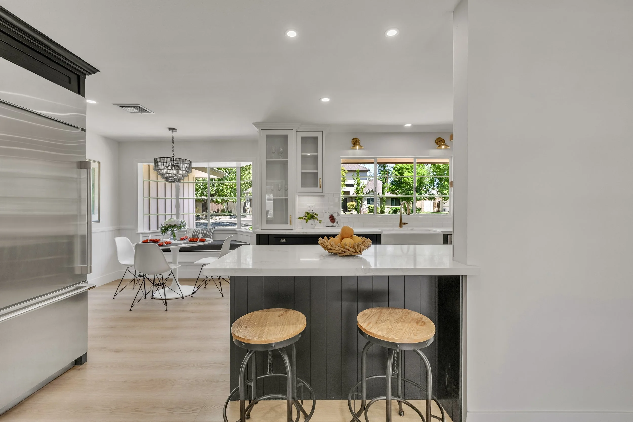 This bright, modern kitchen with a breakfast nook boasts large windows and sleek appliances in Phoenix, AZ, captured with expert real estate photography to highlight its inviting design and natural light.