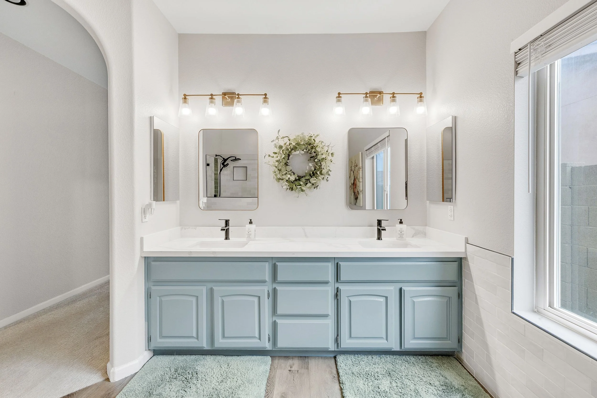 This Goodyear, AZ bathroom features a bright double sink vanity with light blue cabinets and large mirrors, captured in stunning real estate photography to highlight its clean and modern design.