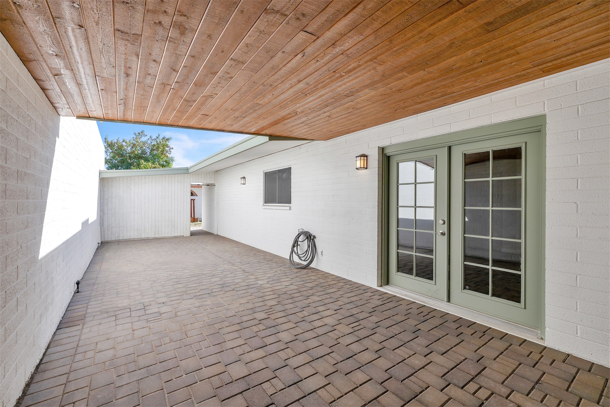 This covered outdoor patio area features brick flooring and French doors, captured with professional real estate photography in Tempe, AZ.