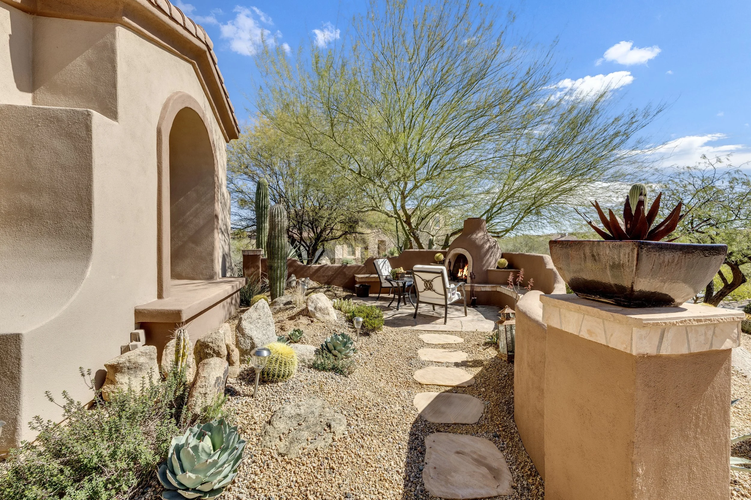 This Scottsdale, AZ home features a desert-style patio with a stone pathway, outdoor fireplace, and vibrant succulent garden, perfectly captured with expert real estate photography.