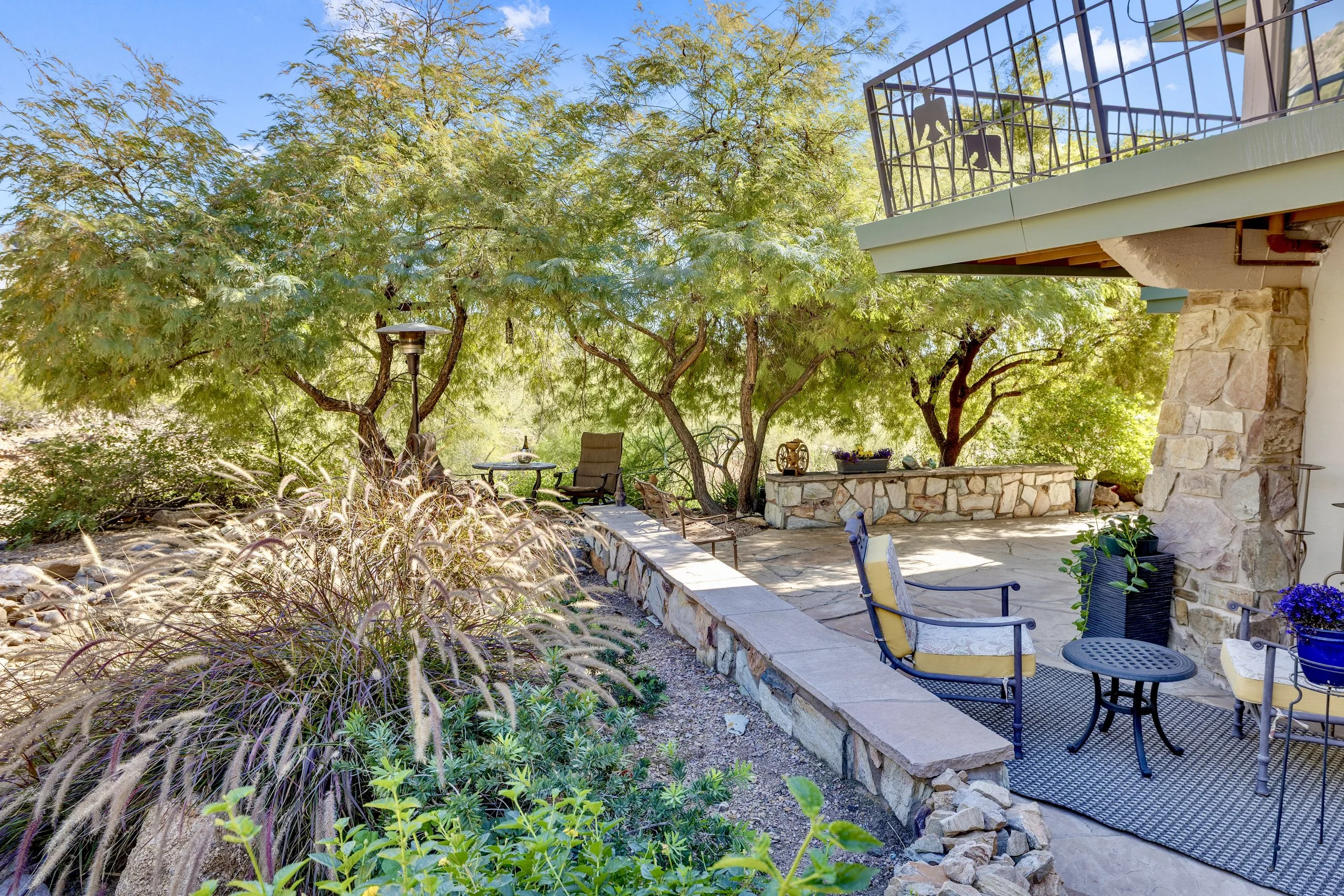 This outdoor patio features a stone wall, comfortable seating, and lush greenery, showcasing beautiful real estate photography in Paradise Valley, AZ.